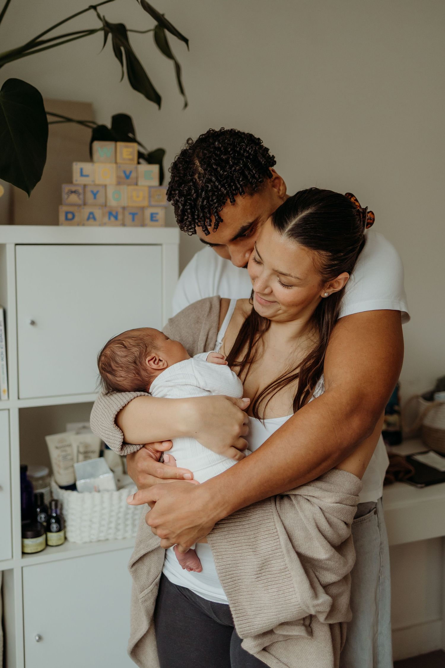 Interracial couple embracing while holding their newborn baby Dante.