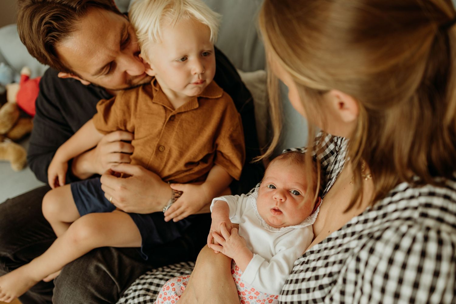 Family with toddler and newborn baby sitting together on a couch.