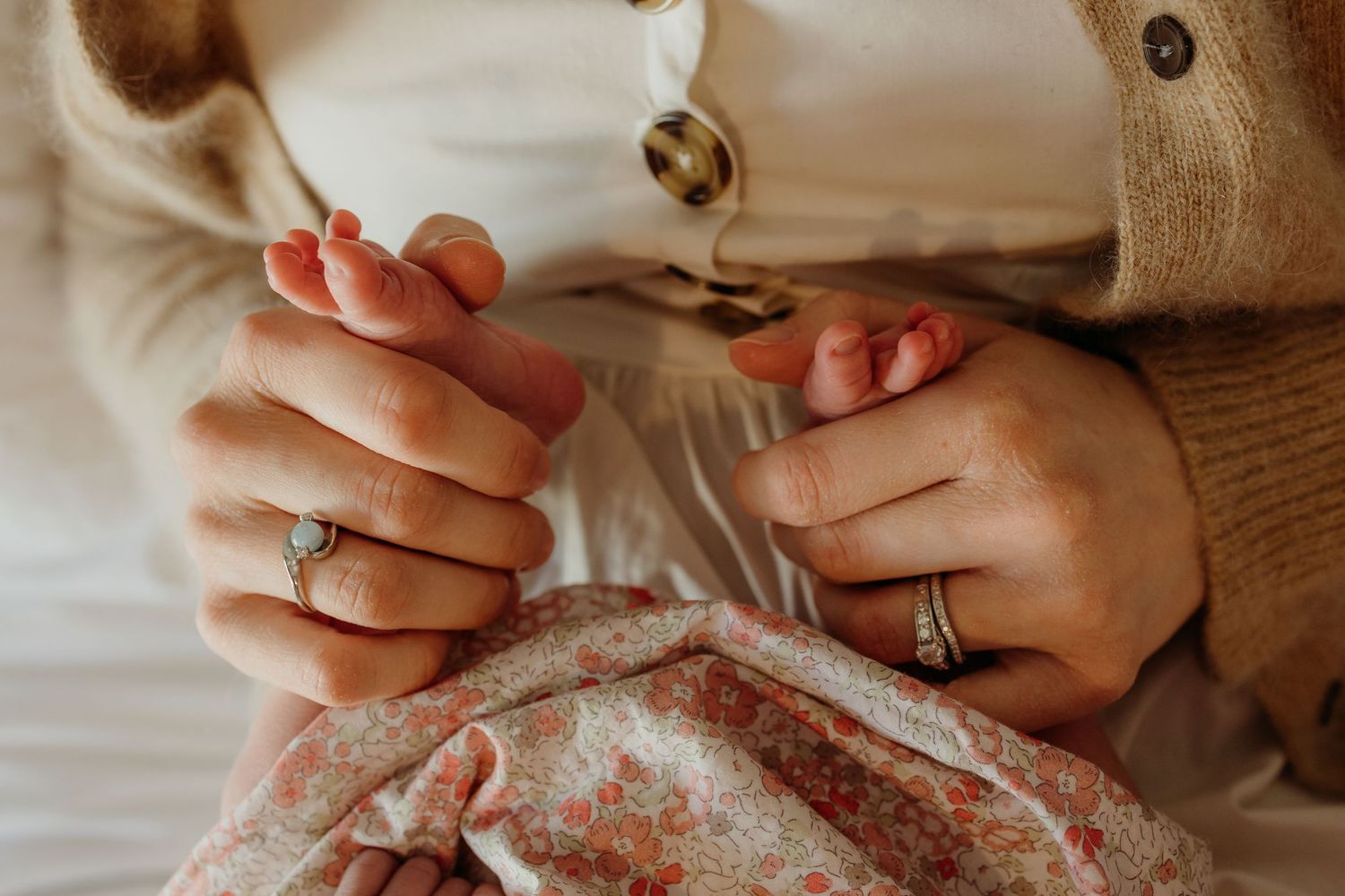 Close-up of a mother holding her newborn baby's tiny hands while wearing rings.