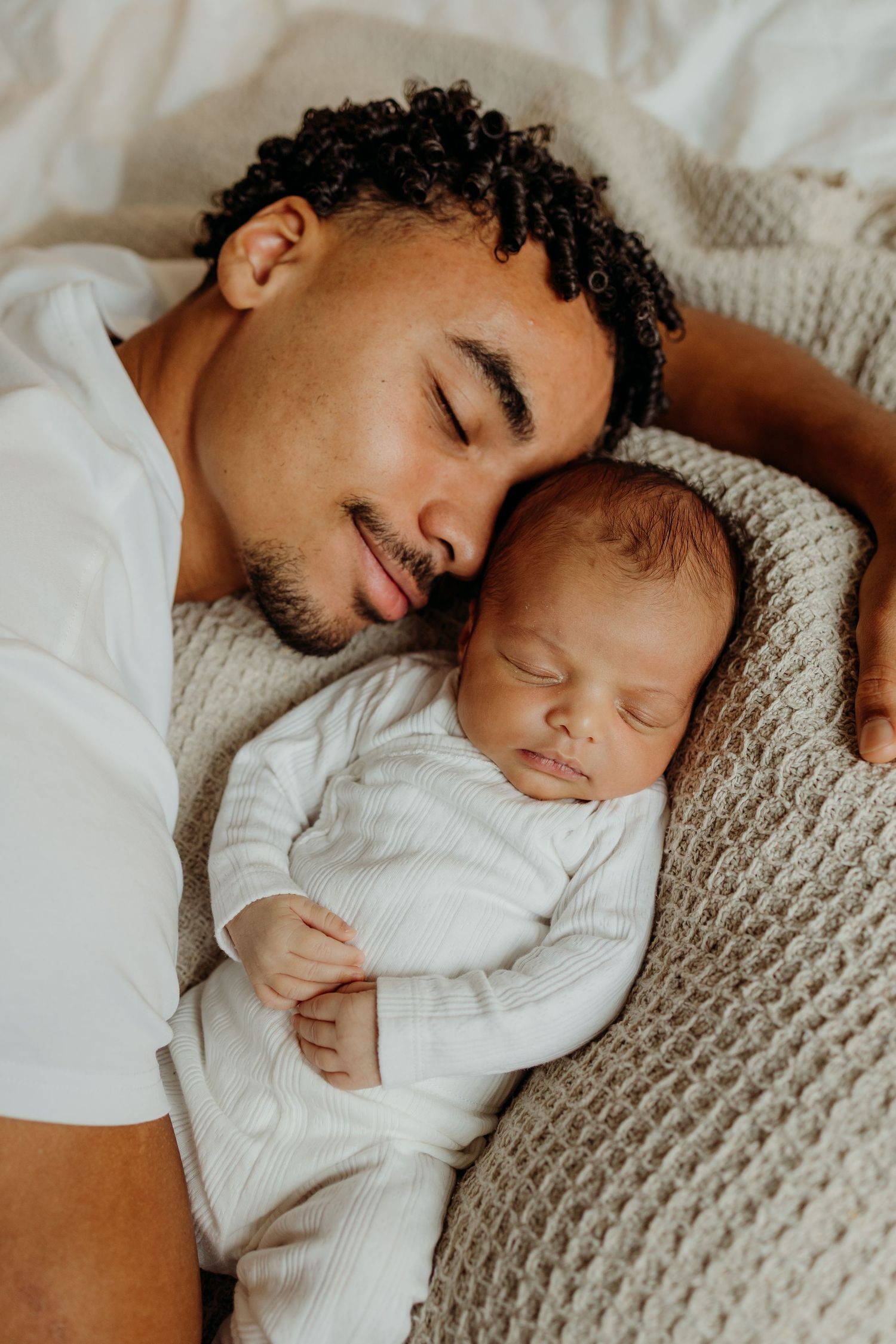 Smiling father lying beside his peacefully sleeping newborn baby.