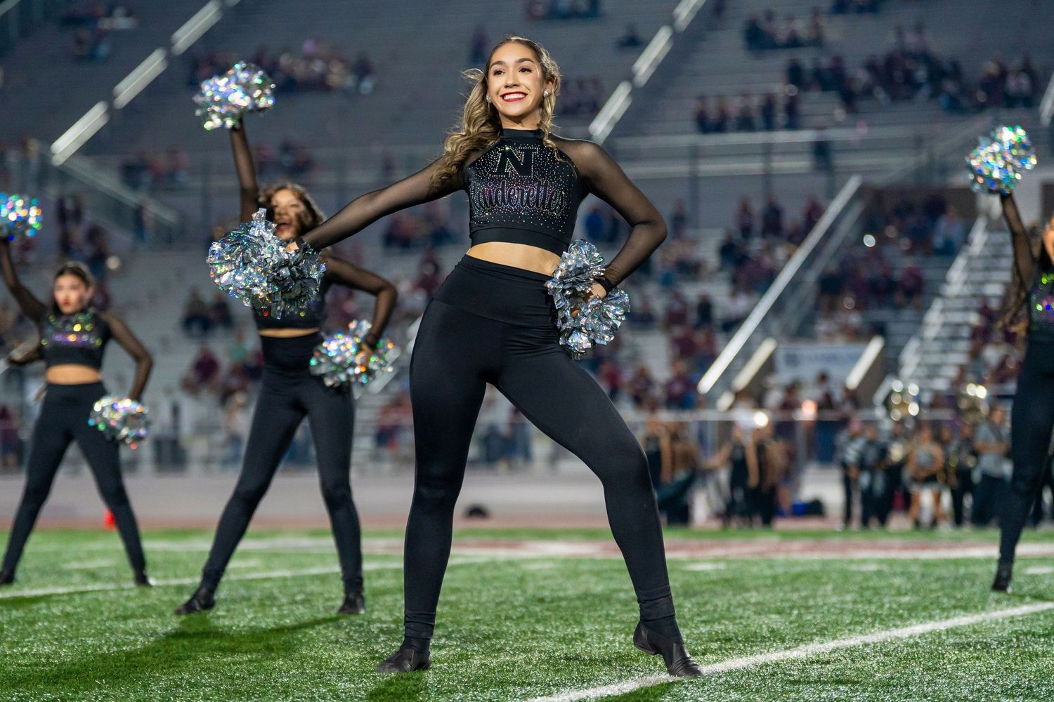 Dance team performer with pom-poms smiling during a stadium performance