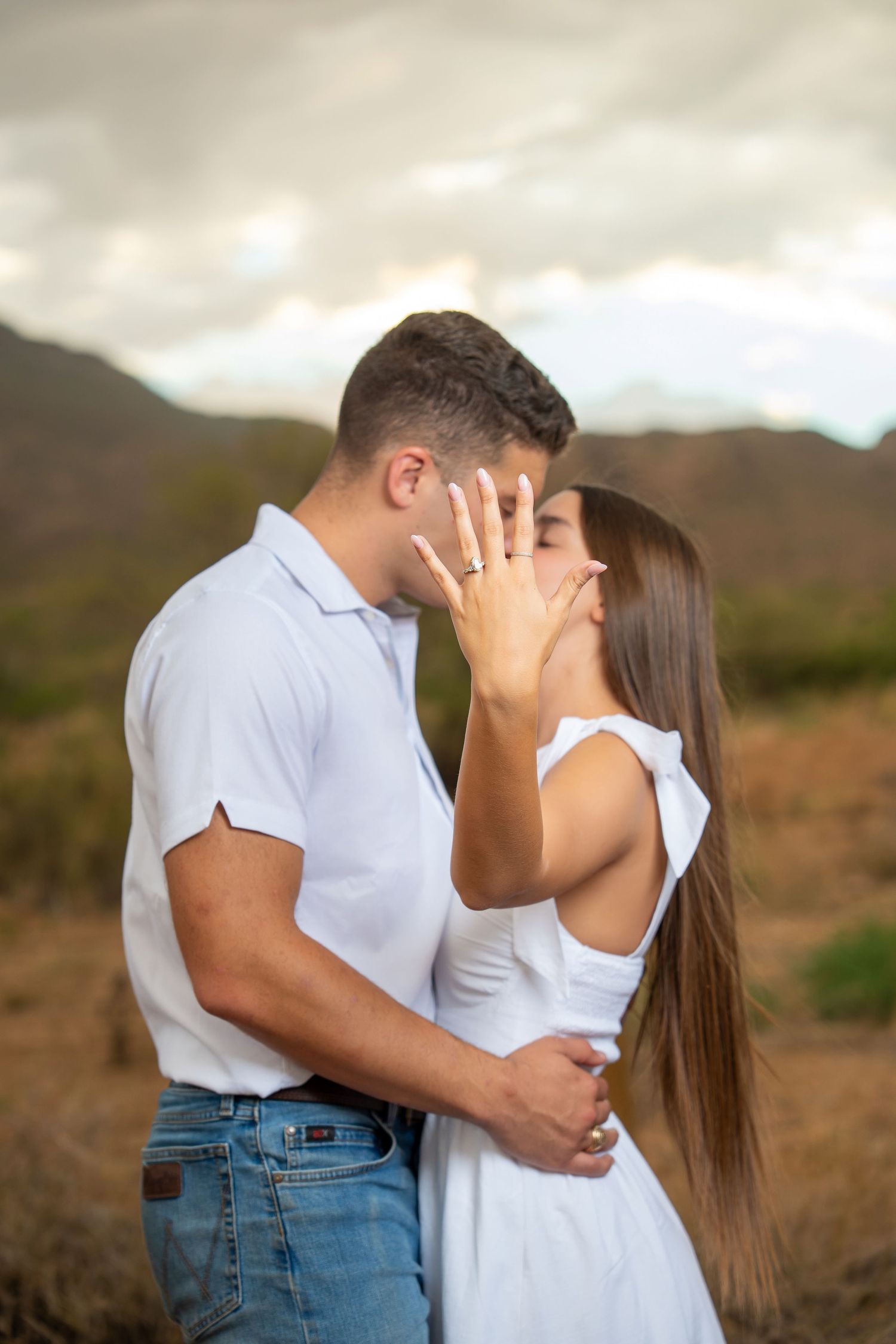Bride-to-be showing her engagement ring while kissing her fiancé outdoors