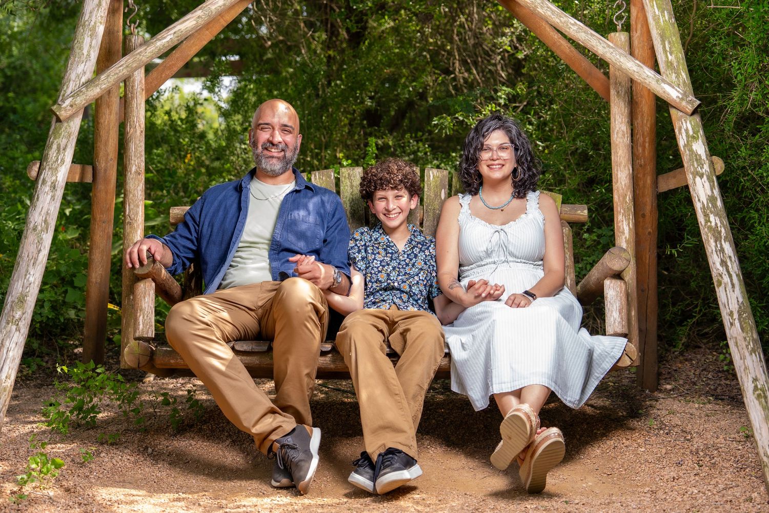 Family of three smiling together on a wooden swing during an outdoor family session