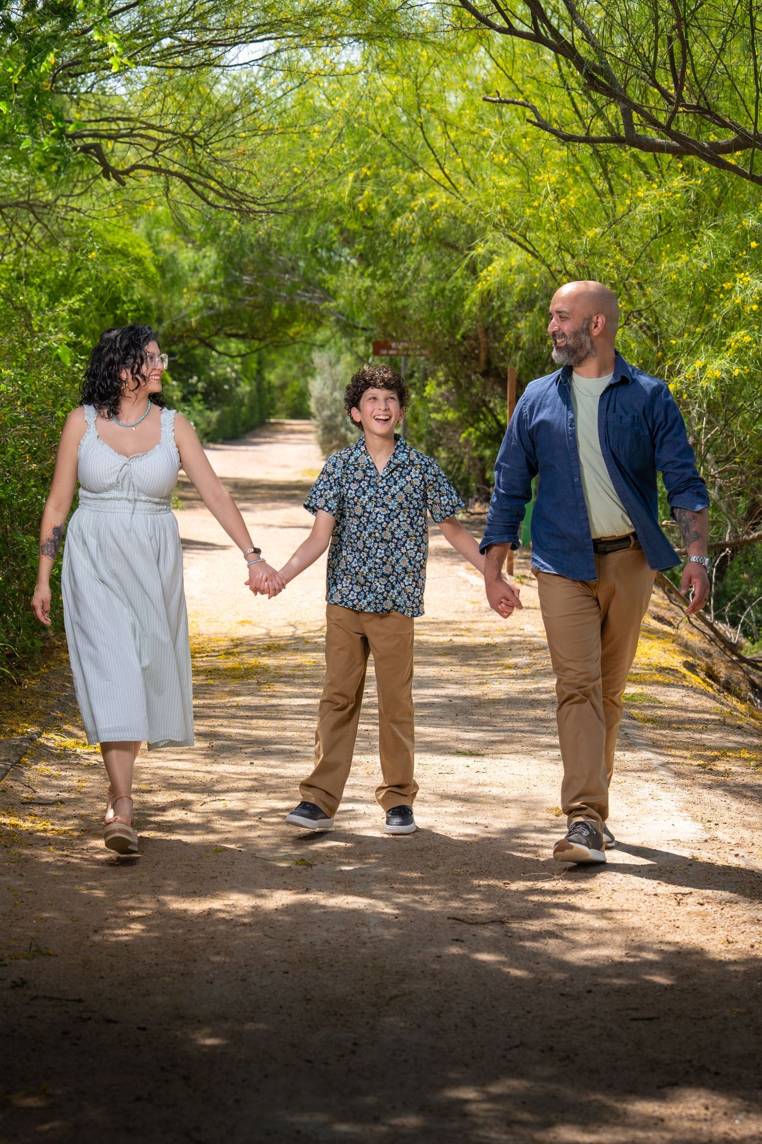 Family of three walking together on a tree-lined trail during an outdoor portrait session