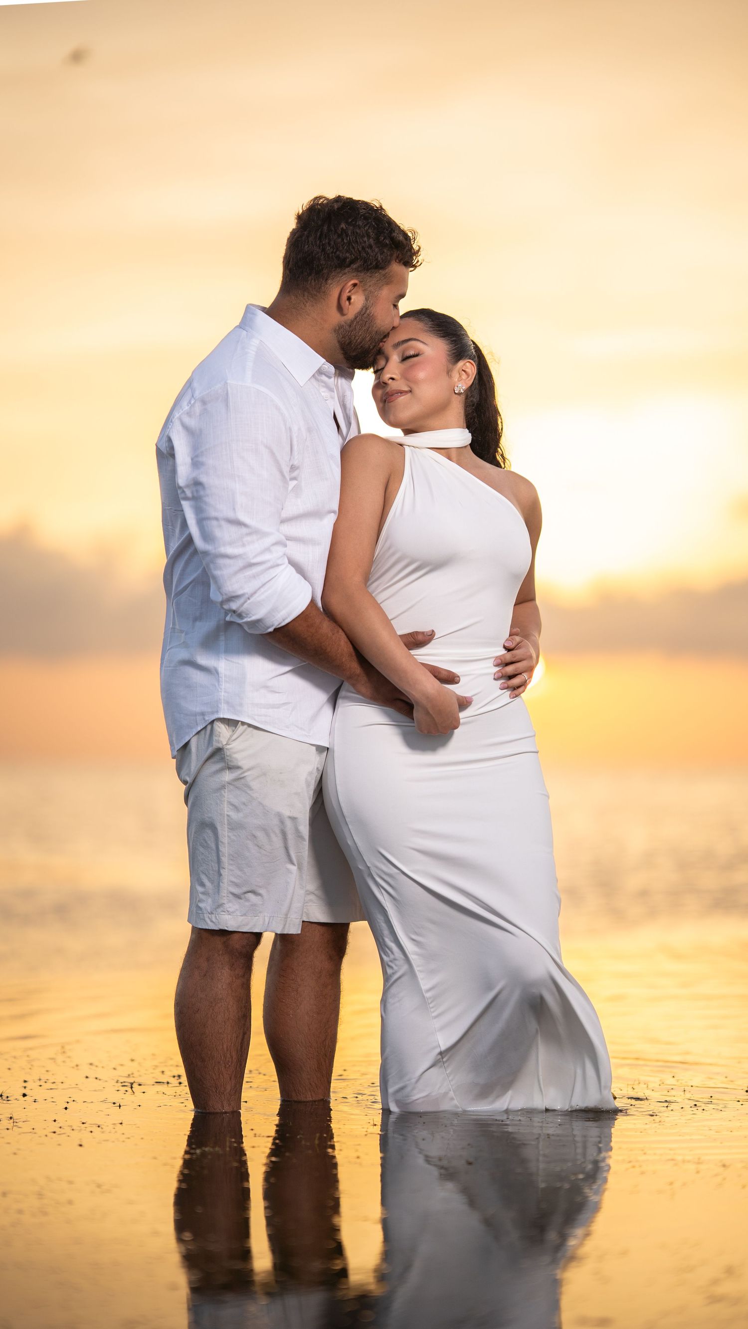 Couple holding hands in shallow ocean water during a sunset photoshoot