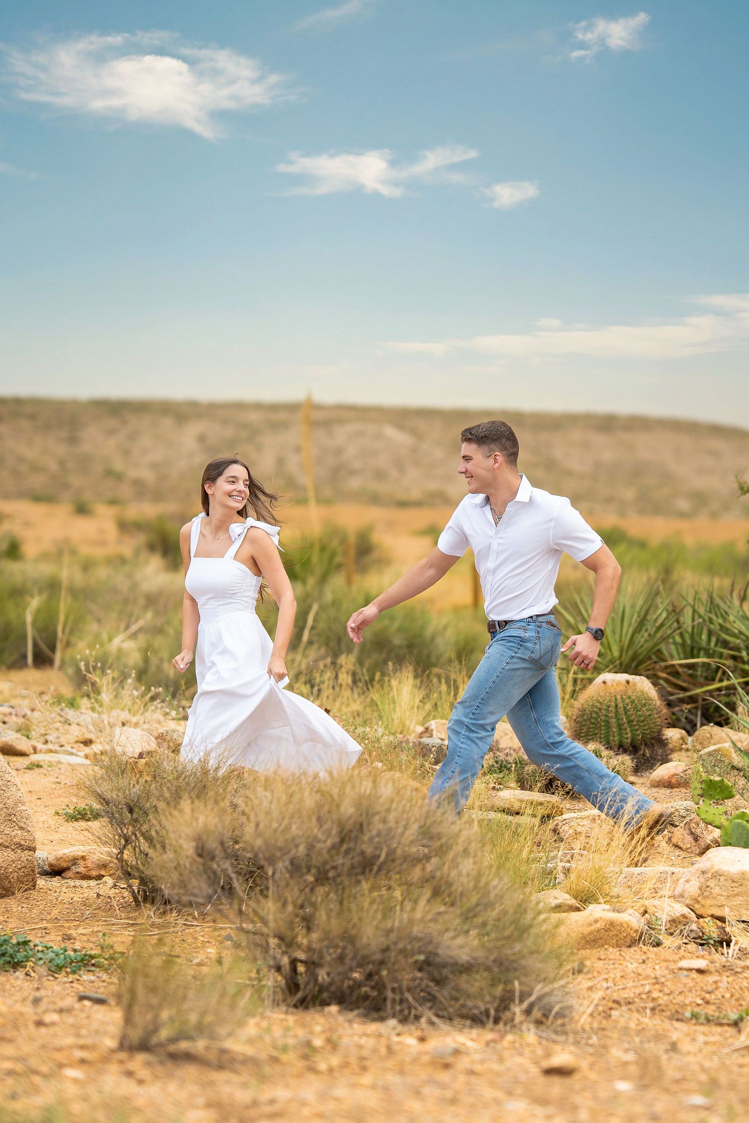 Engaged couple running and laughing together through a desert landscape