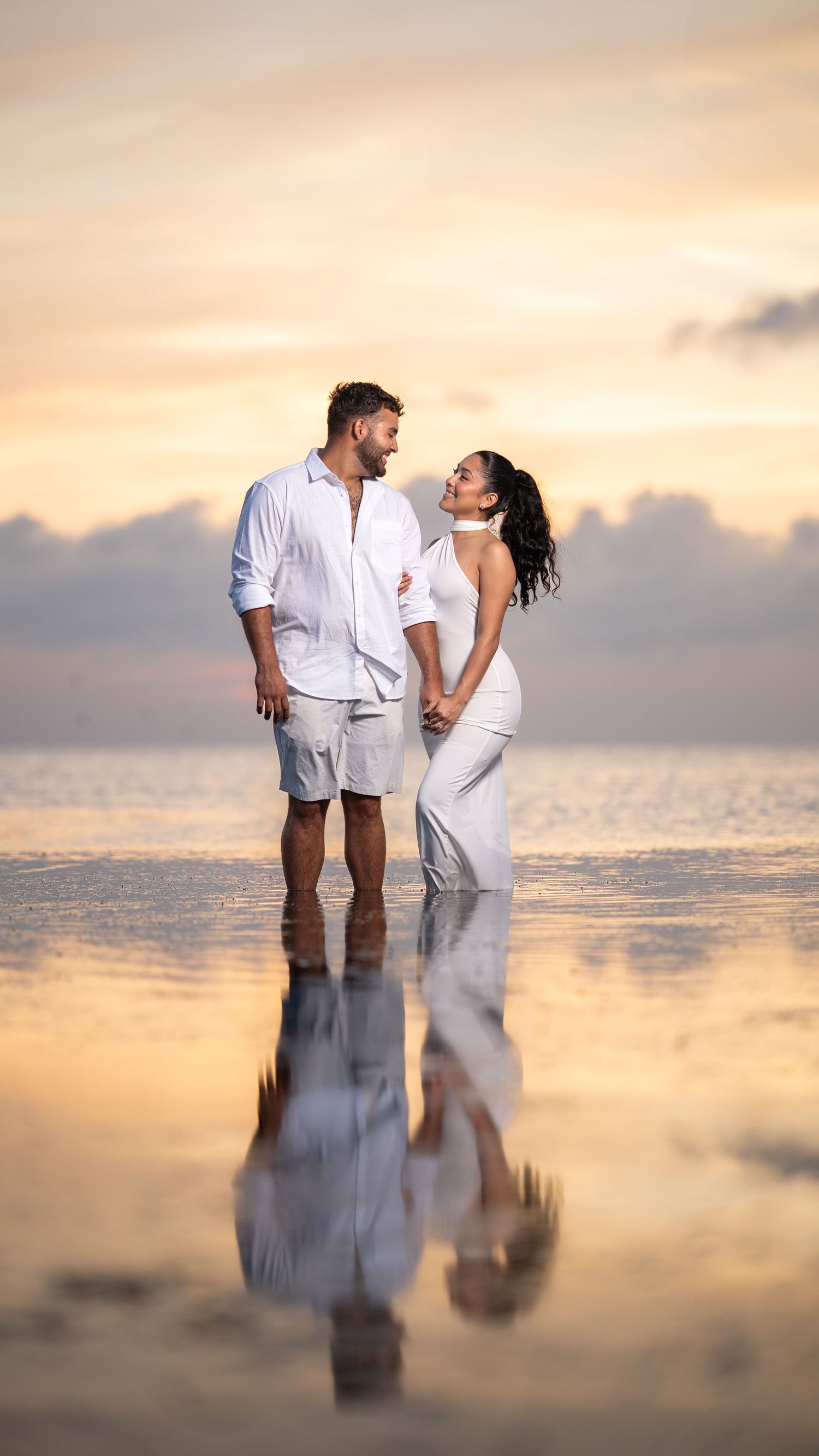 Couple embracing in shallow ocean water during a romantic sunset session