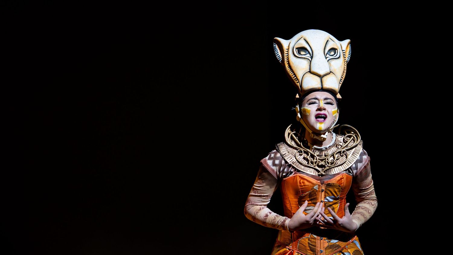 Musical theater performer in a colorful animal costume performing under dramatic stage lights