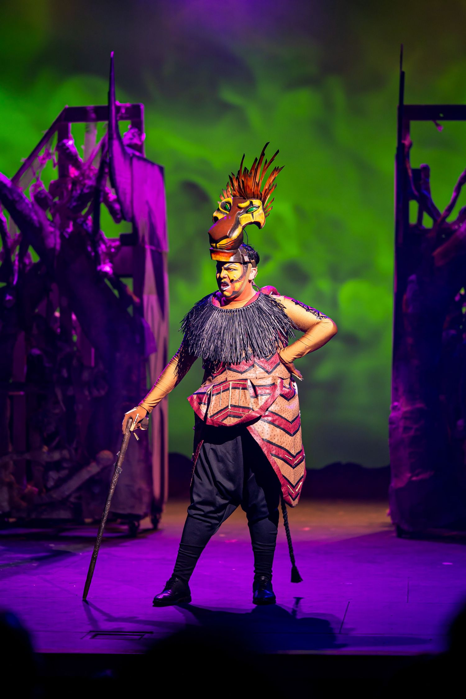 Musical theater performer in an elaborate lion costume singing under a spotlight