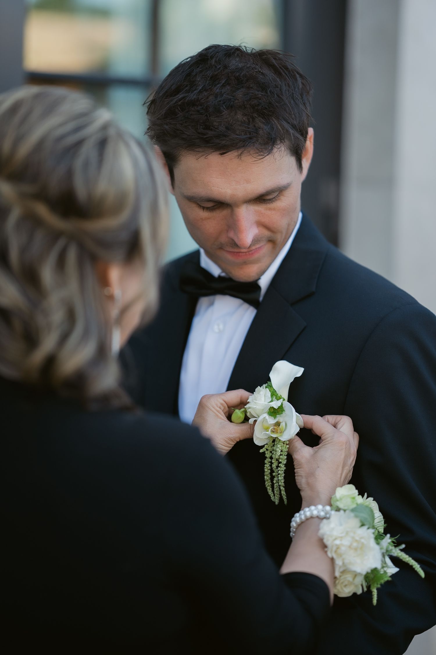Groom in black tuxedo having white floral boutonniere pinned on lapel.