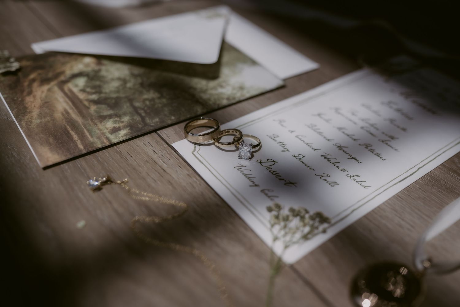 Wedding rings rest on elegant stationery with floral envelope and jewelry in a styled flat lay detail shot.