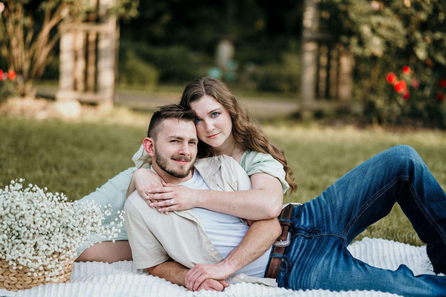 Happy couple cuddling on white blanket in garden with baby's breath flowers in warm sunlight.