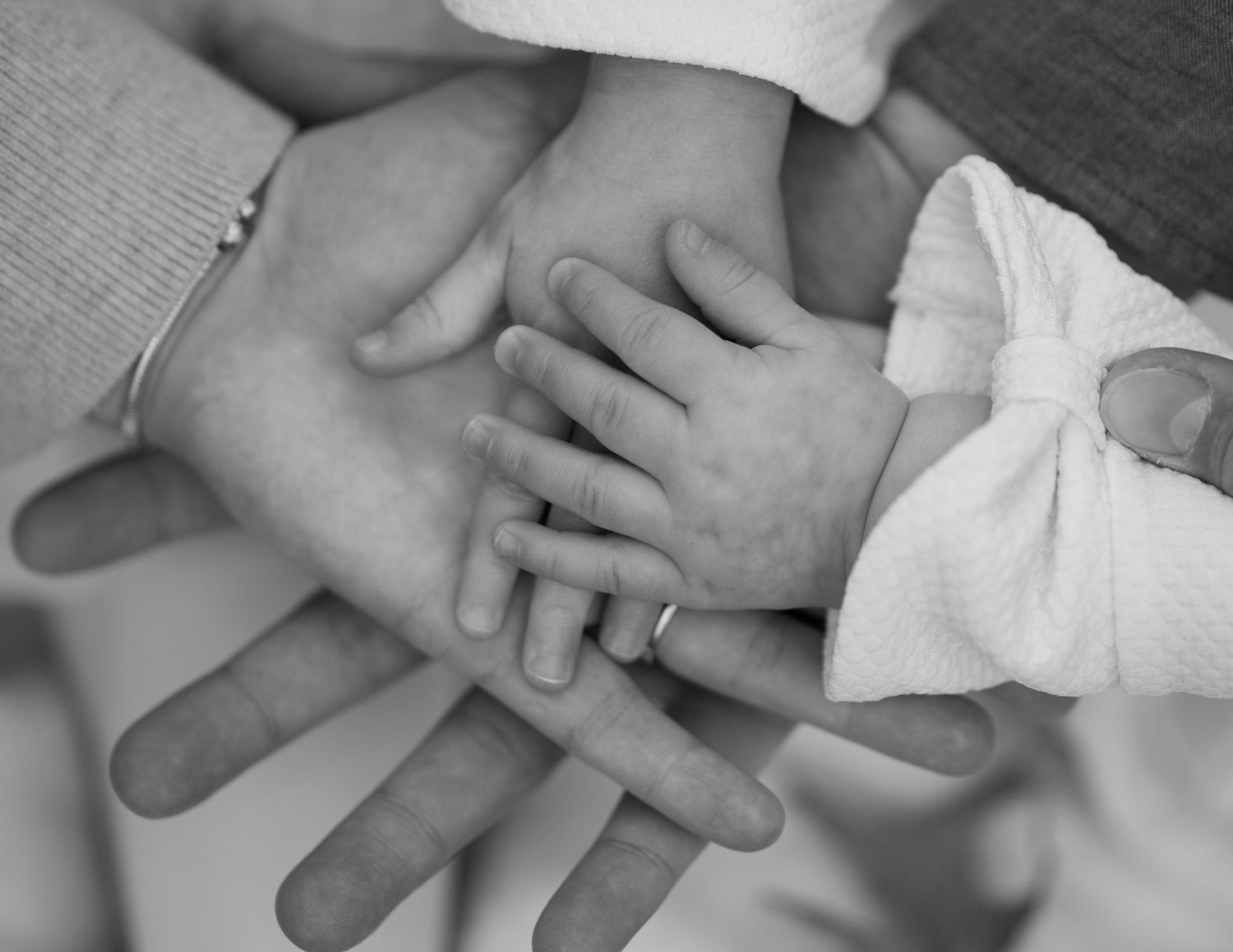 Black and white close-up of family hands stacked together including newborn baby hands.
