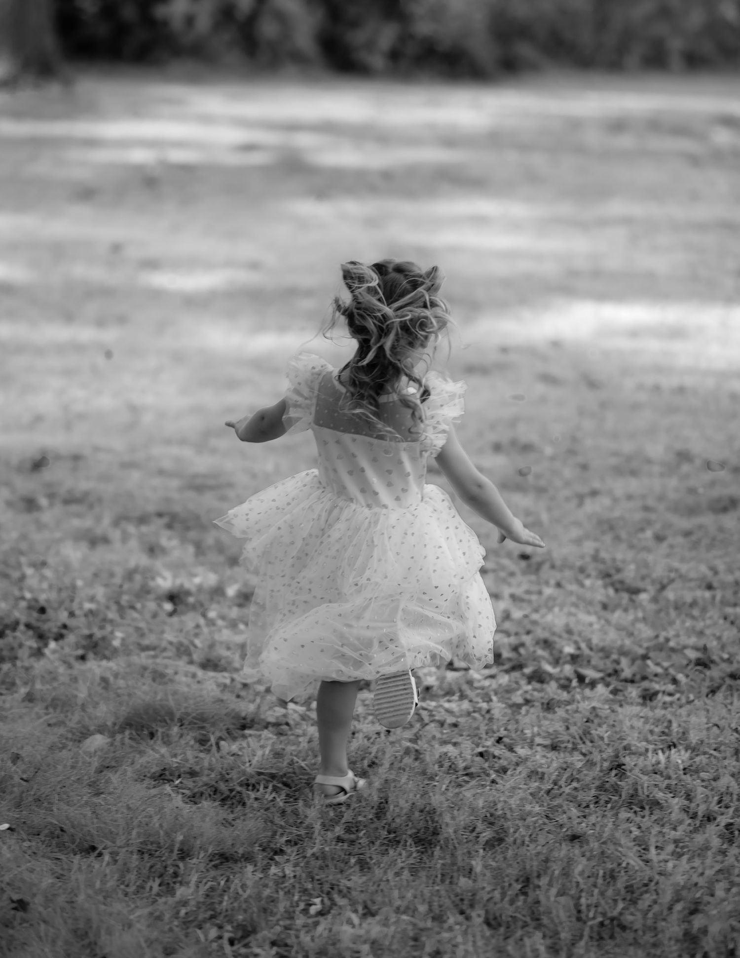 Black and white photo of young girl in white lace dress running through grassy field.