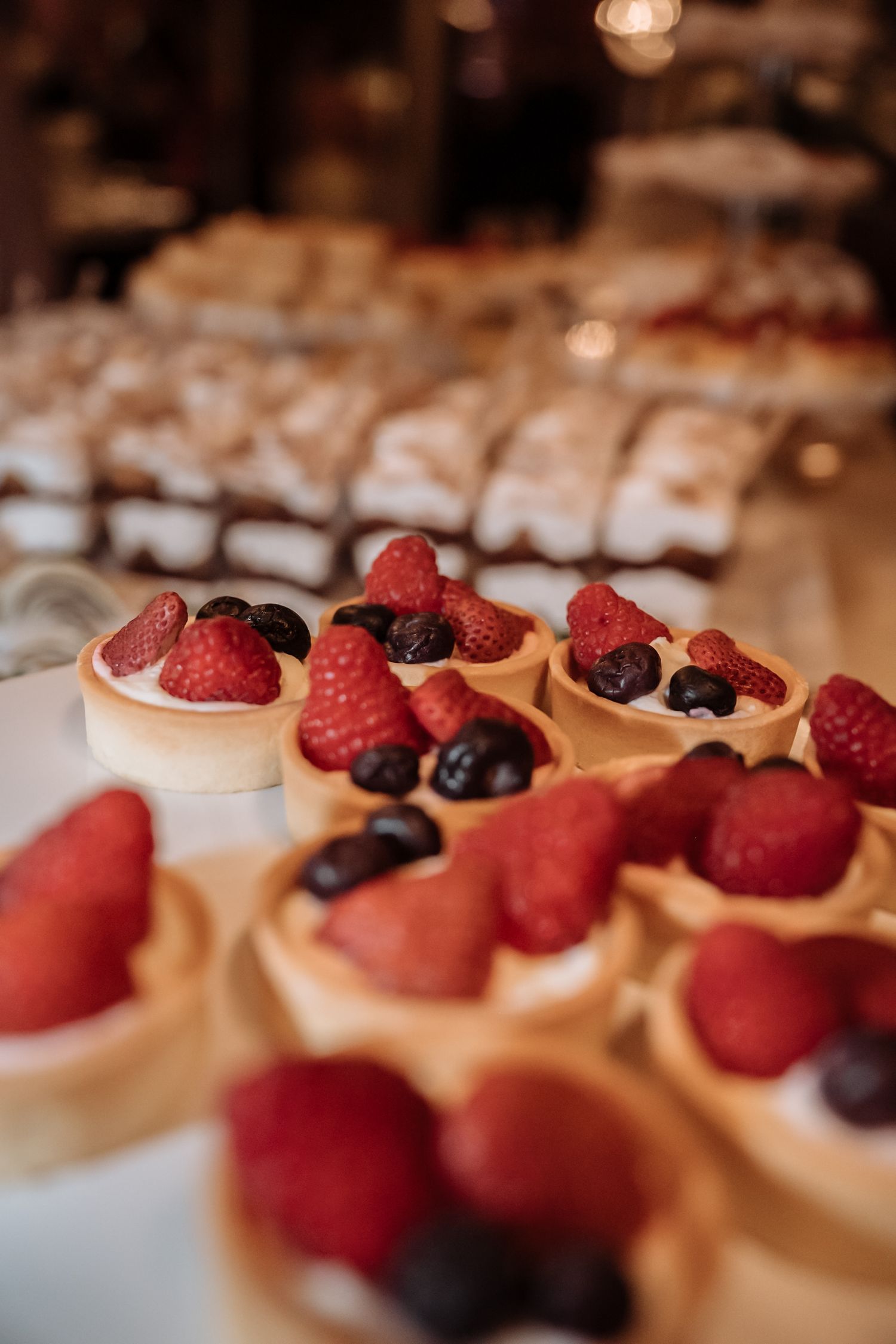 Fresh strawberry and blueberry tarts with cream filling displayed on a dessert table at an elegant event.