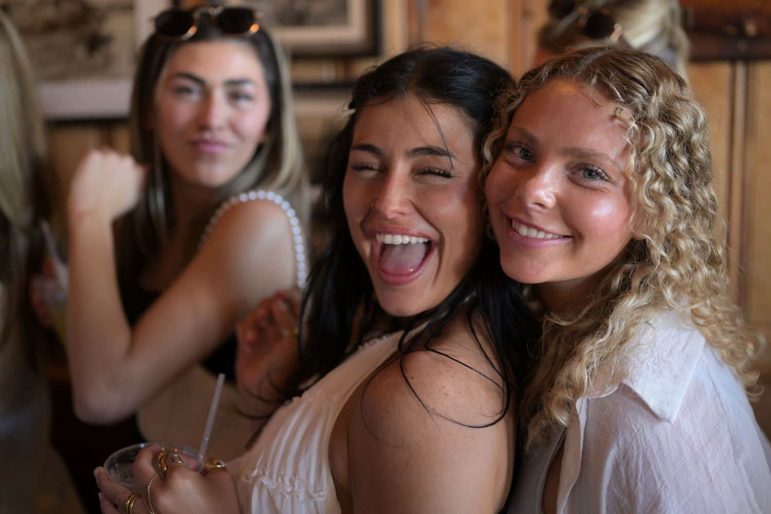 Three young women smiling and posing together at a party, one sticking out her tongue playfully.