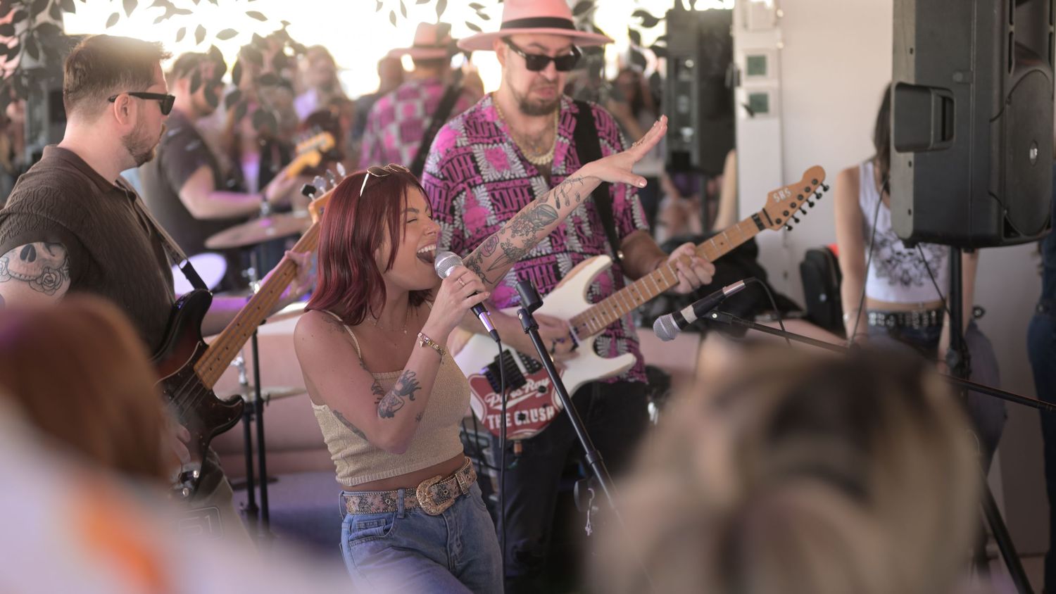 Live band performing outdoors with female singer and guitarist in colorful shirt at a sunny music event.