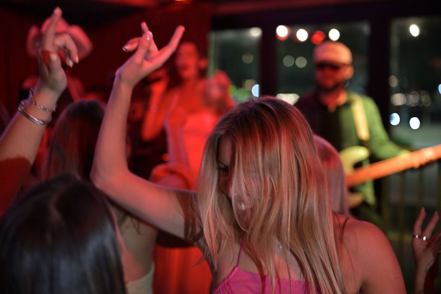 Woman with blonde hair dancing at a lively indoor live music concert under red lights.