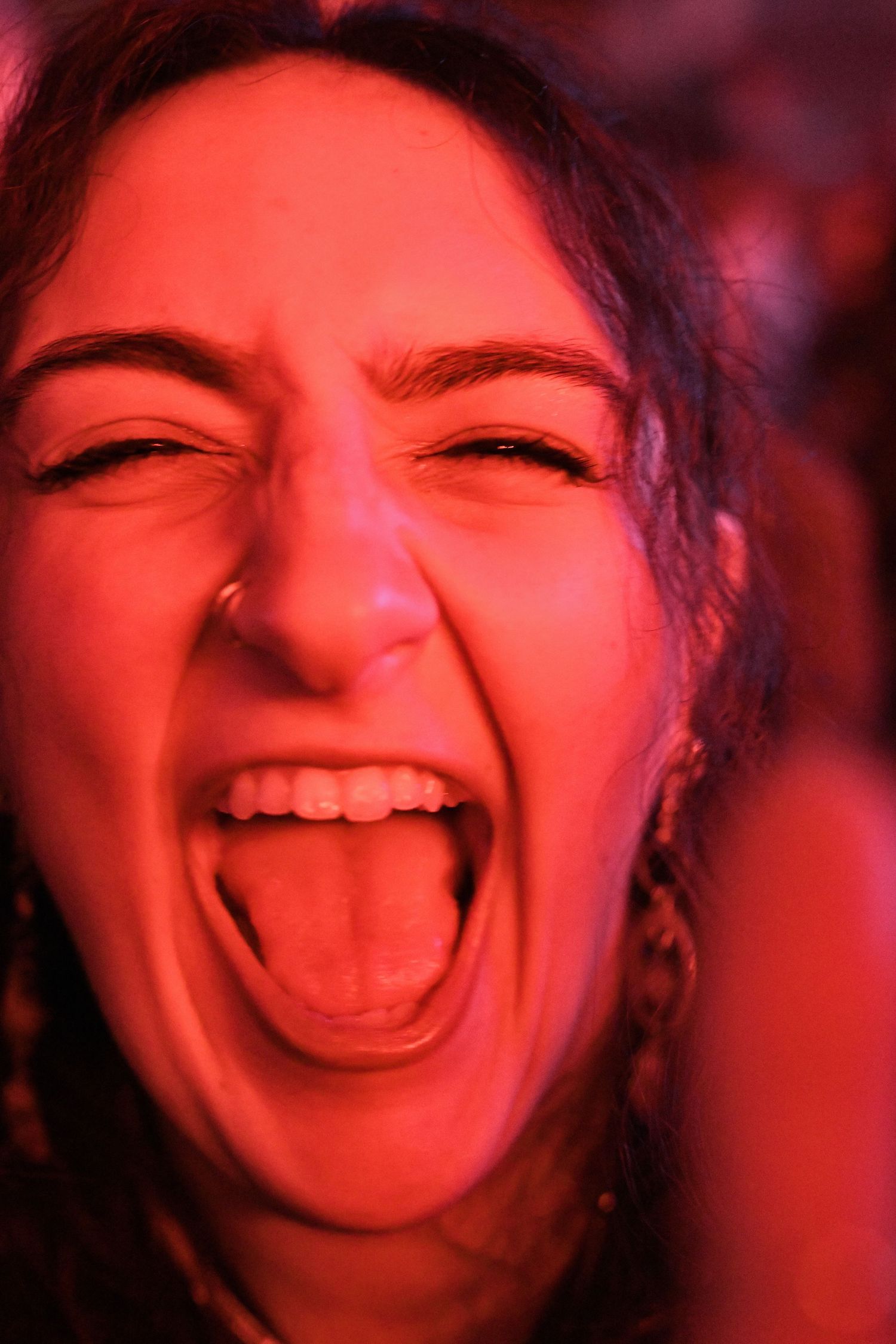 Young woman screaming with mouth wide open, illuminated by vibrant red lighting at a concert or party.