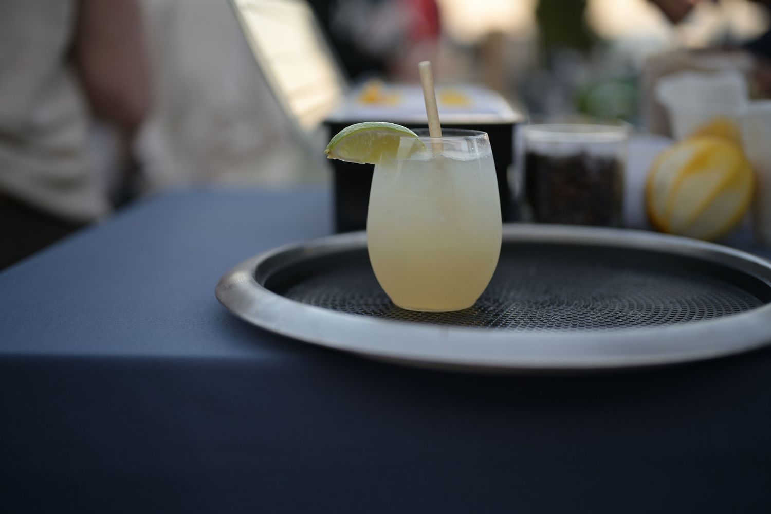 A refreshing lemon margarita cocktail with a lime garnish served on a round tray at an outdoor event.
