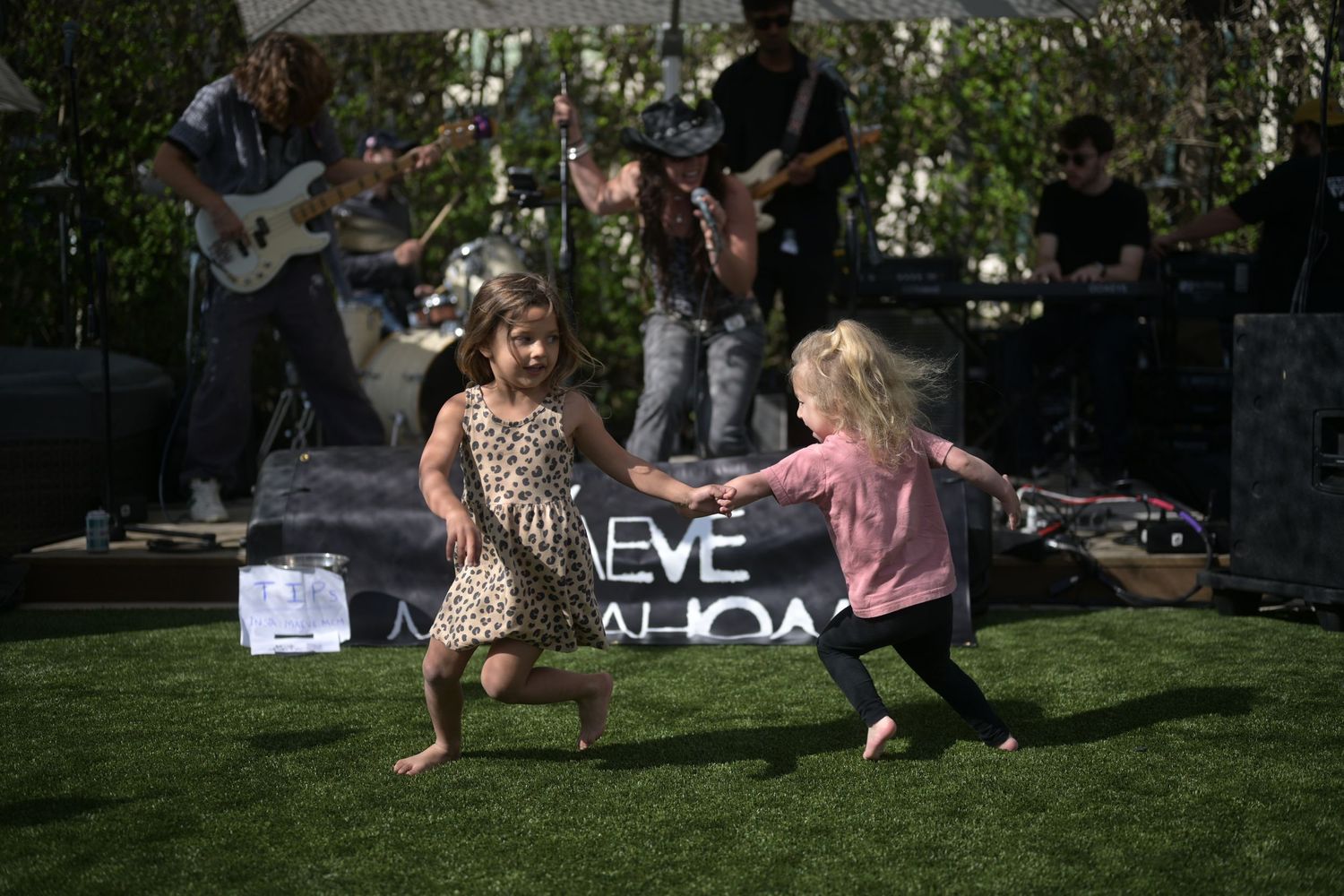 Two young girls dancing together on grass at an outdoor live music concert event.