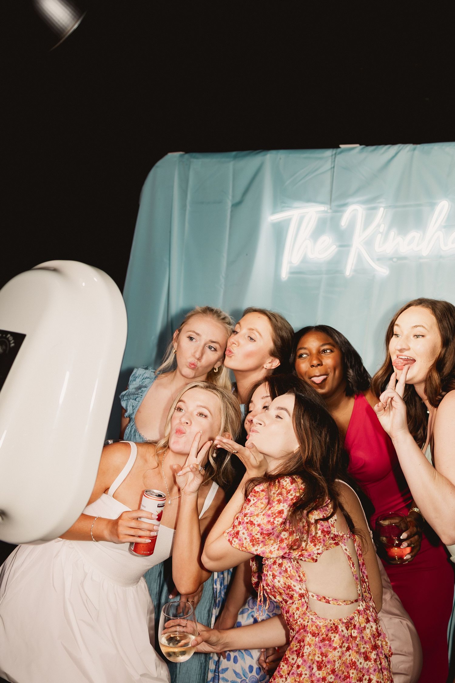 A group of friends laughing and having fun together at a party with light blue walls in the background.