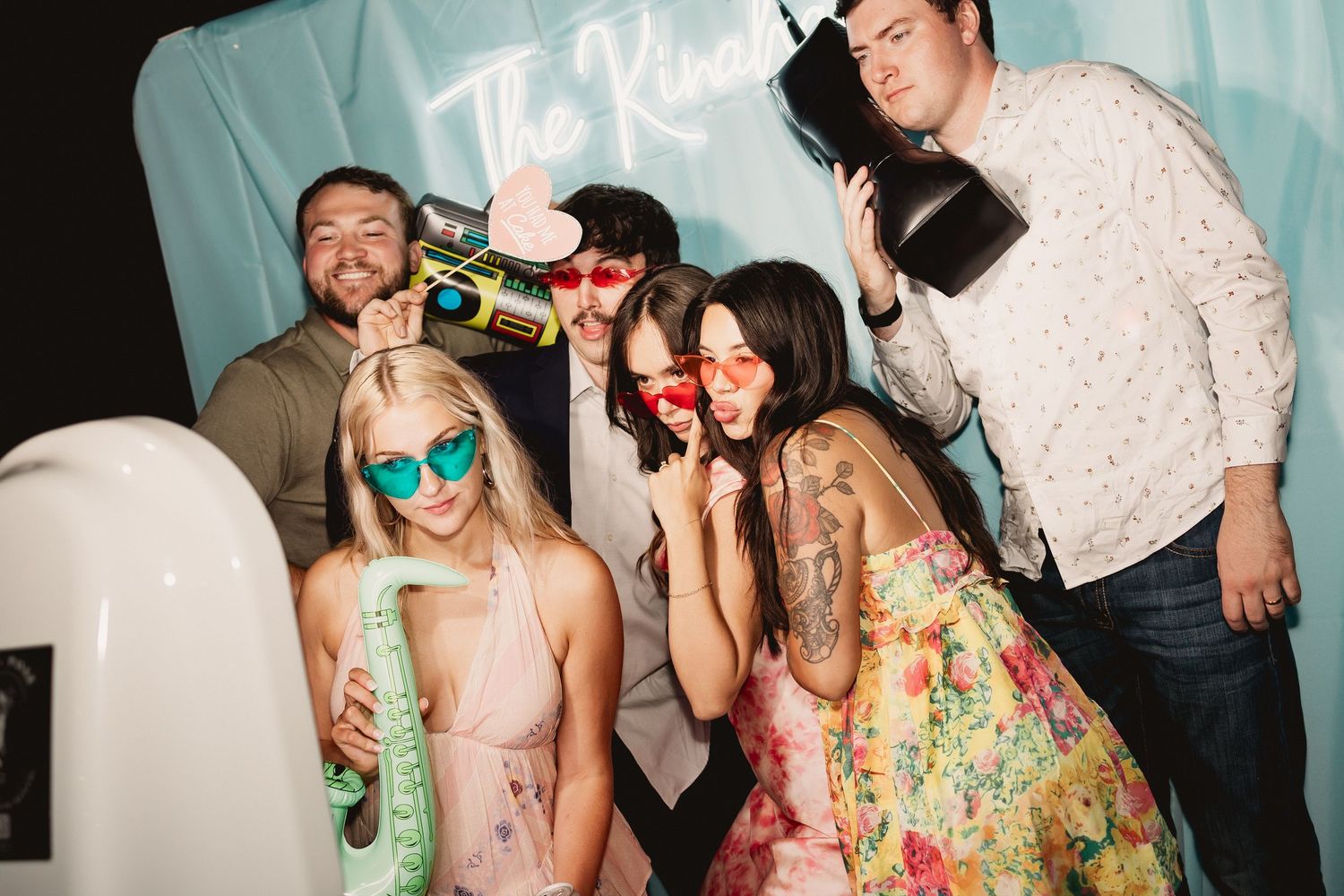 Party guests in colorful floral dresses pose with champagne bottles and glasses at a festive celebration.