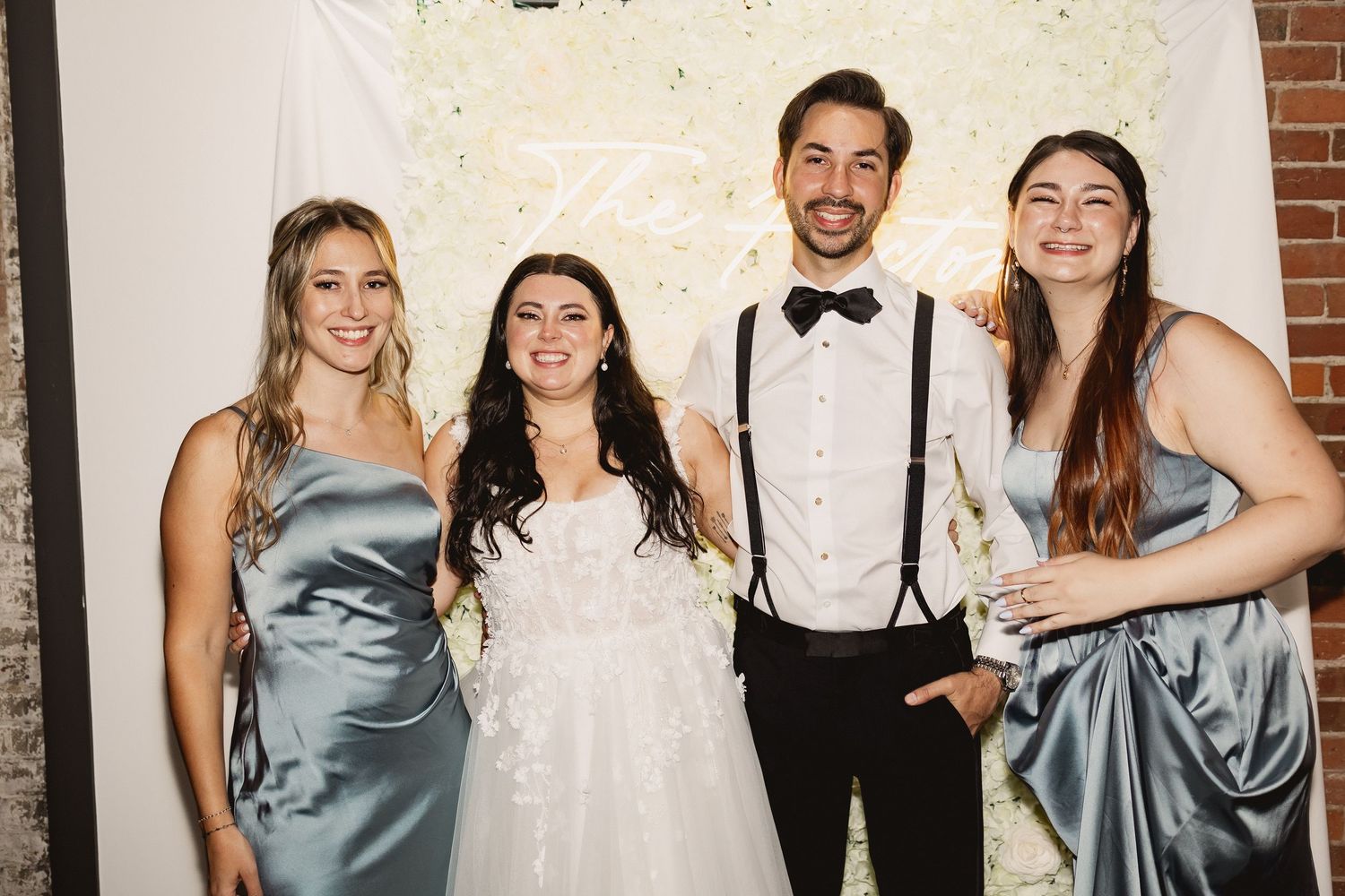 Wedding party members in light blue silk bridesmaid dresses and black bowties pose together at reception.