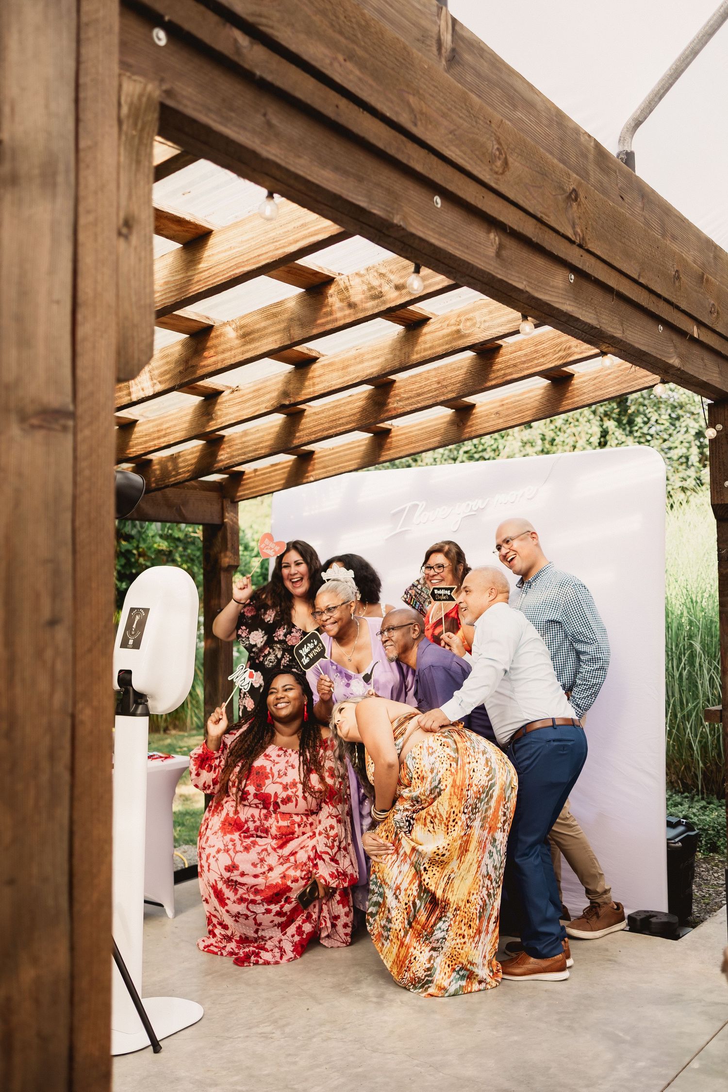 A group poses for photos under a wooden pergola during a festive outdoor gathering.