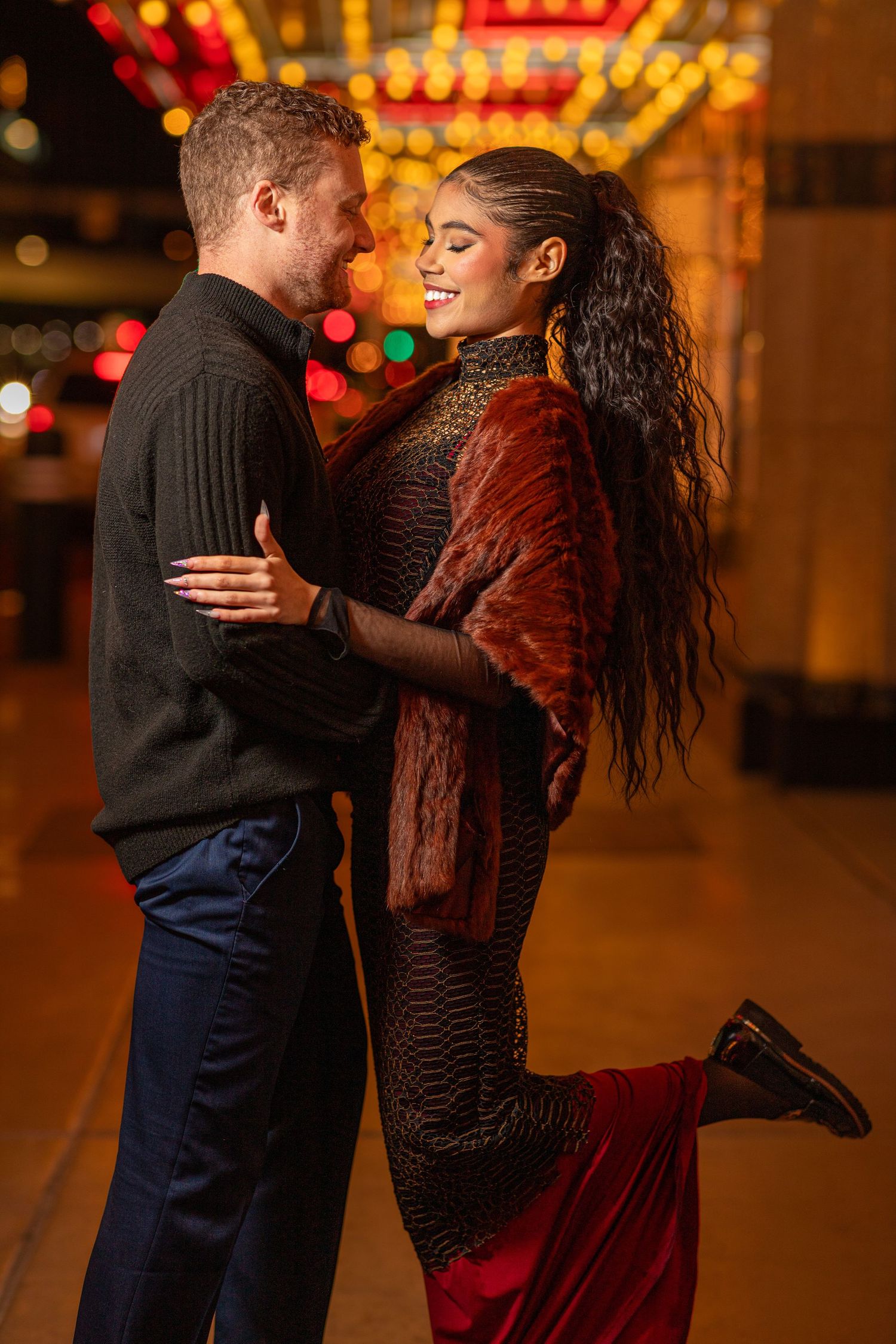 Downtown romance captured at night – vibrant couple’s portrait with glowing marquee lights.
