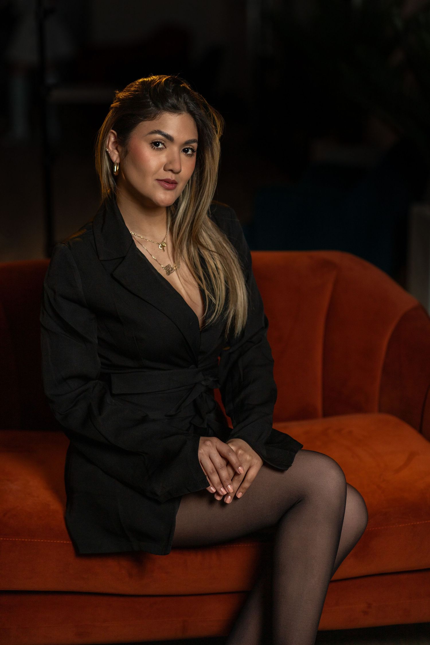 Confident and classy – professional studio portrait of a woman in black on a vibrant orange couch.