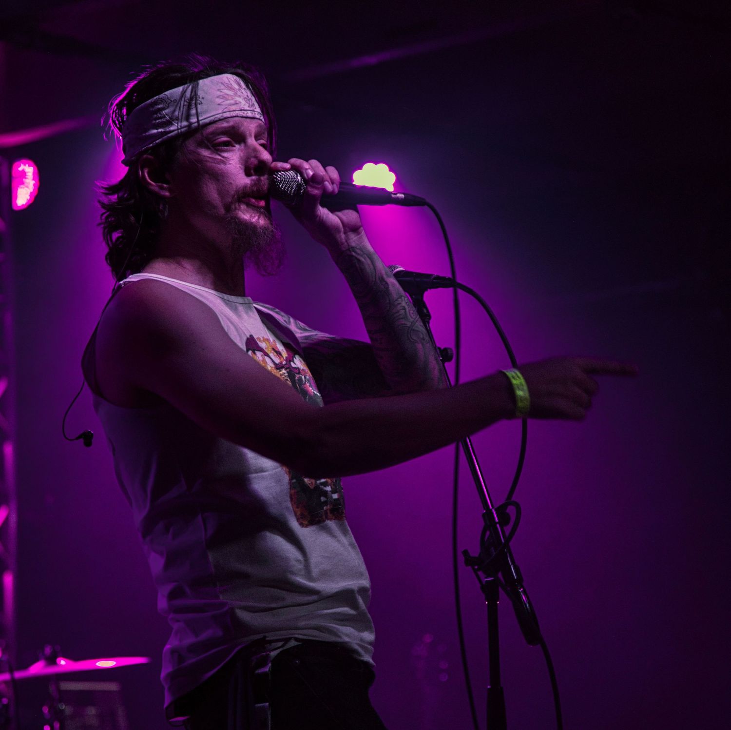 Male rock singer with a bandana performing on stage with microphone, lit by purple stage lights.