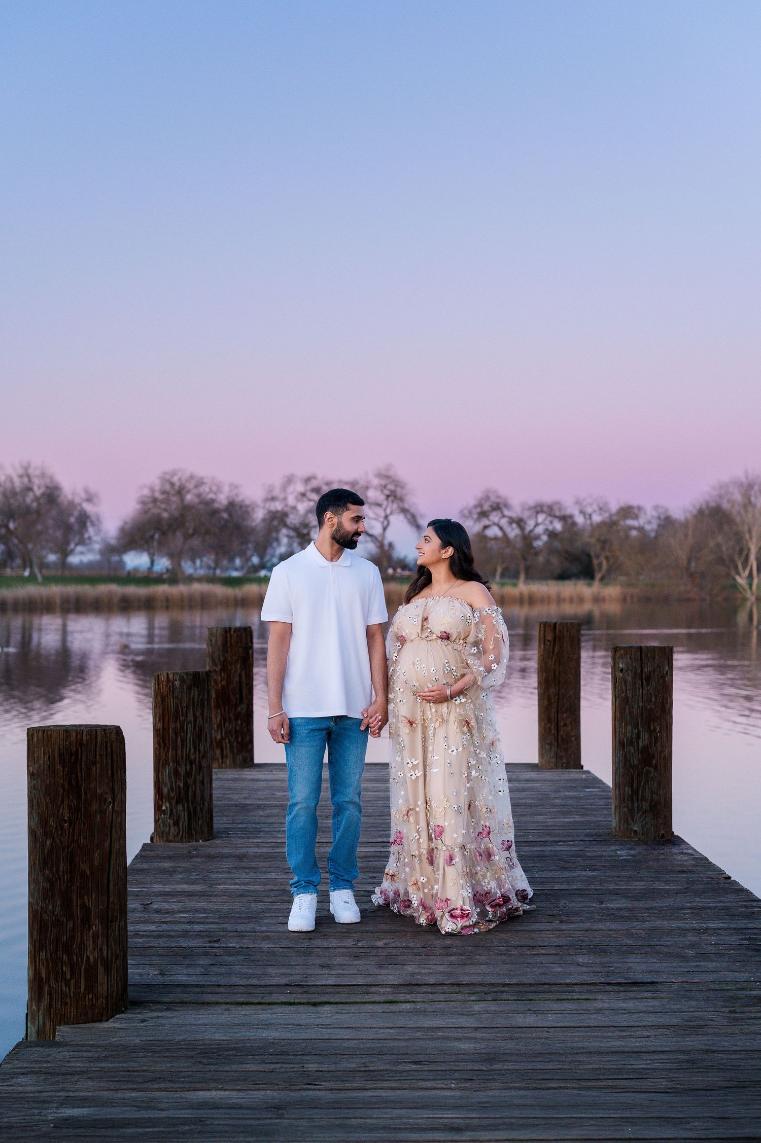 Couple shares intimate moment on wooden pier during sunset maternity session.