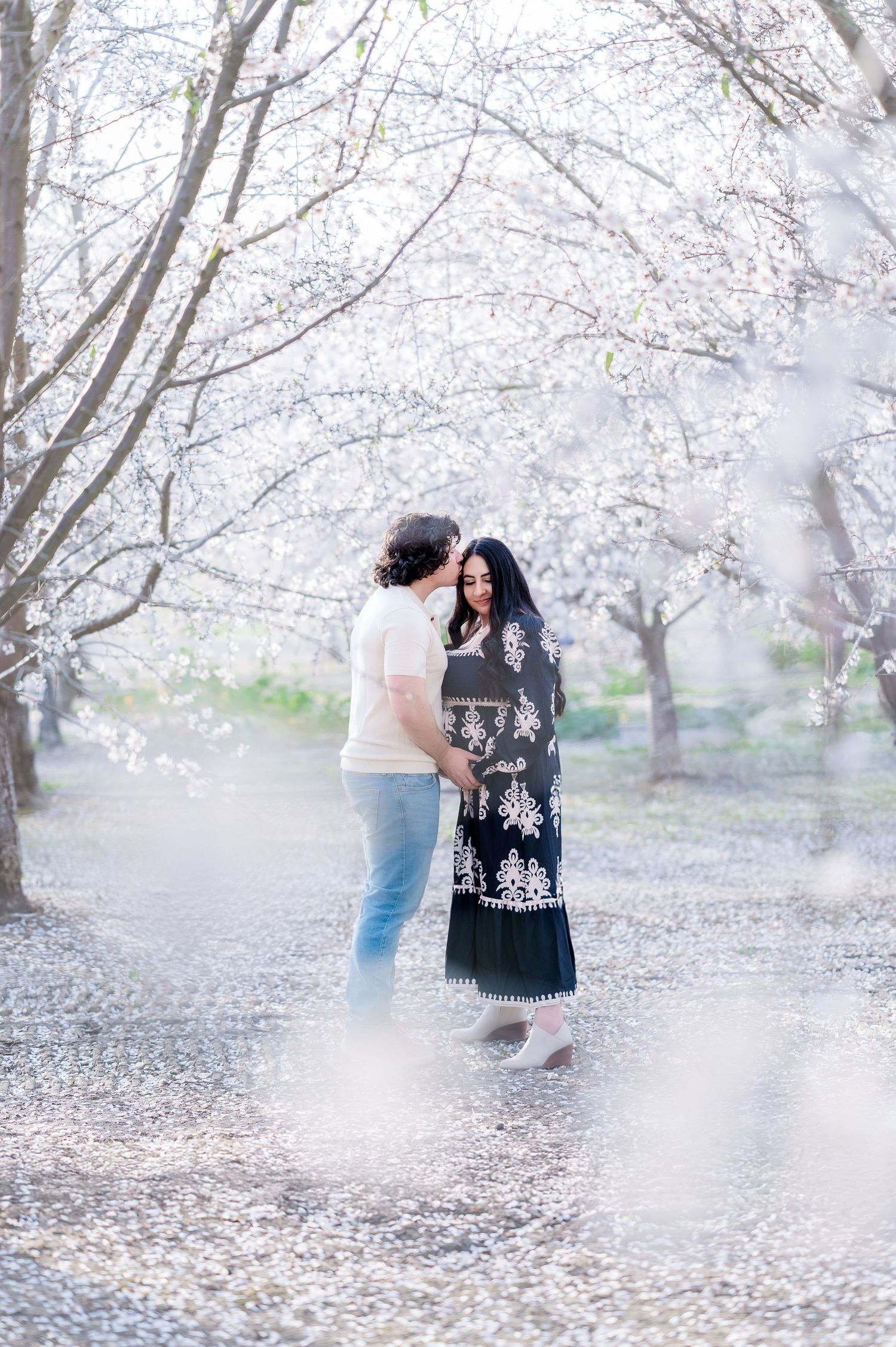 A romantic couple embraces under blooming cherry blossom trees on a misty spring day.