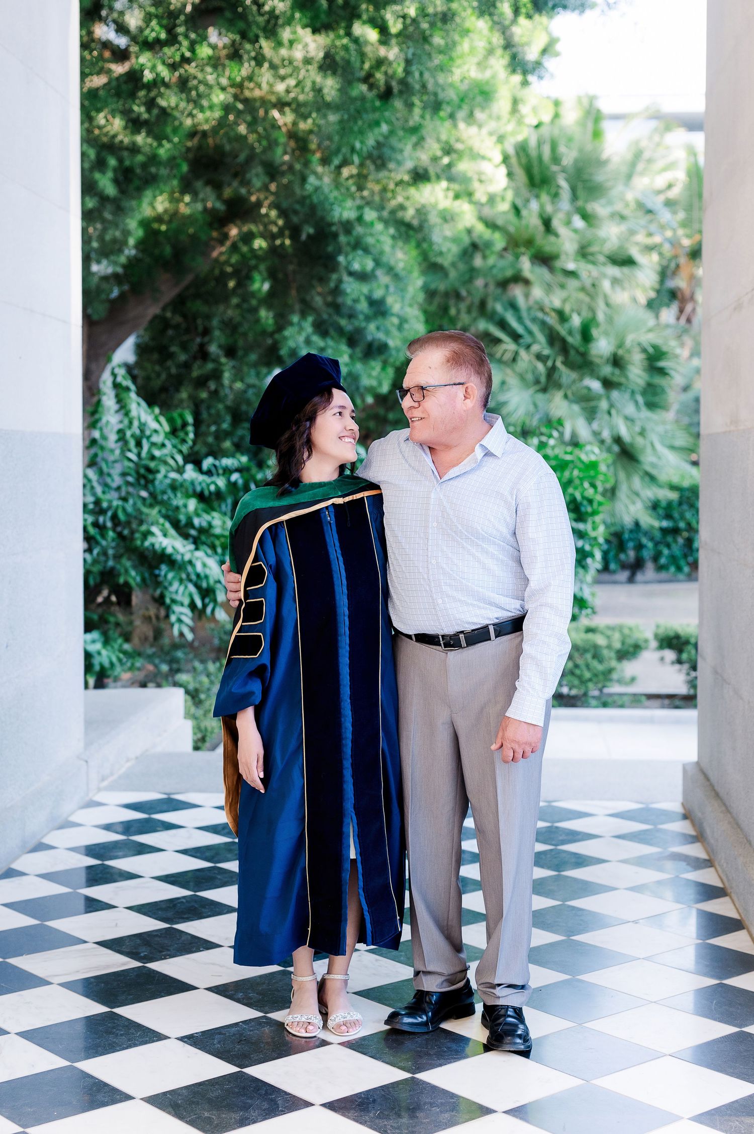 Graduates sharing a moment in a columned hall with black and white checkered floor.
