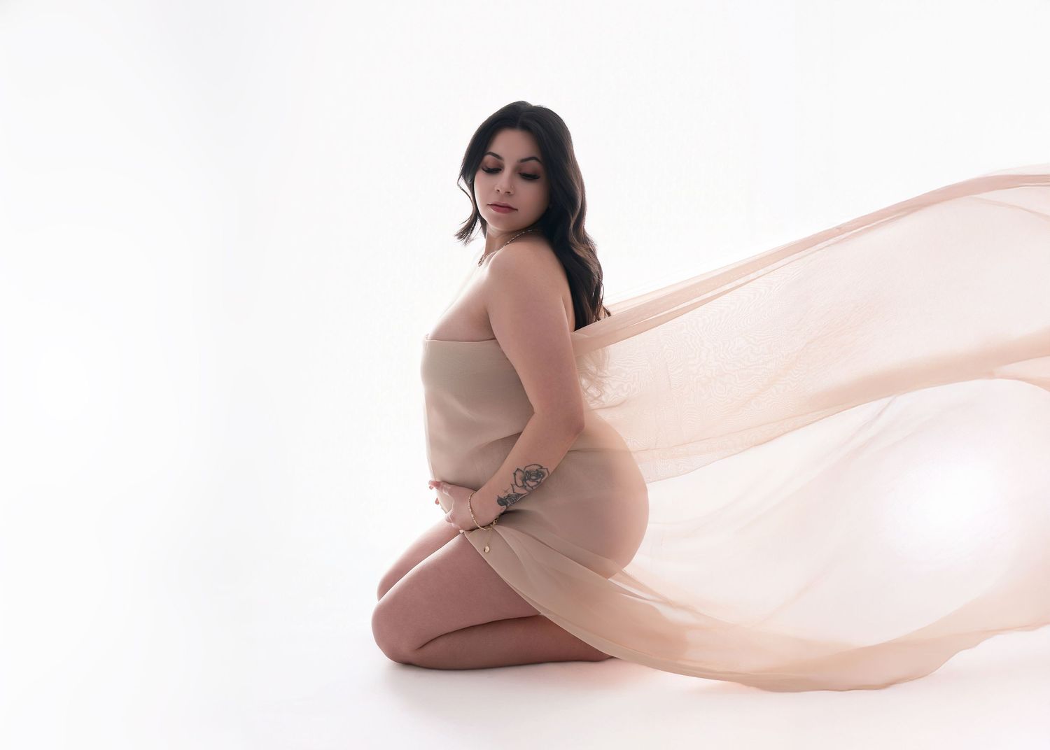 A maternity photo featuring a flowing peach fabric against a white background in an artistic studio setting.