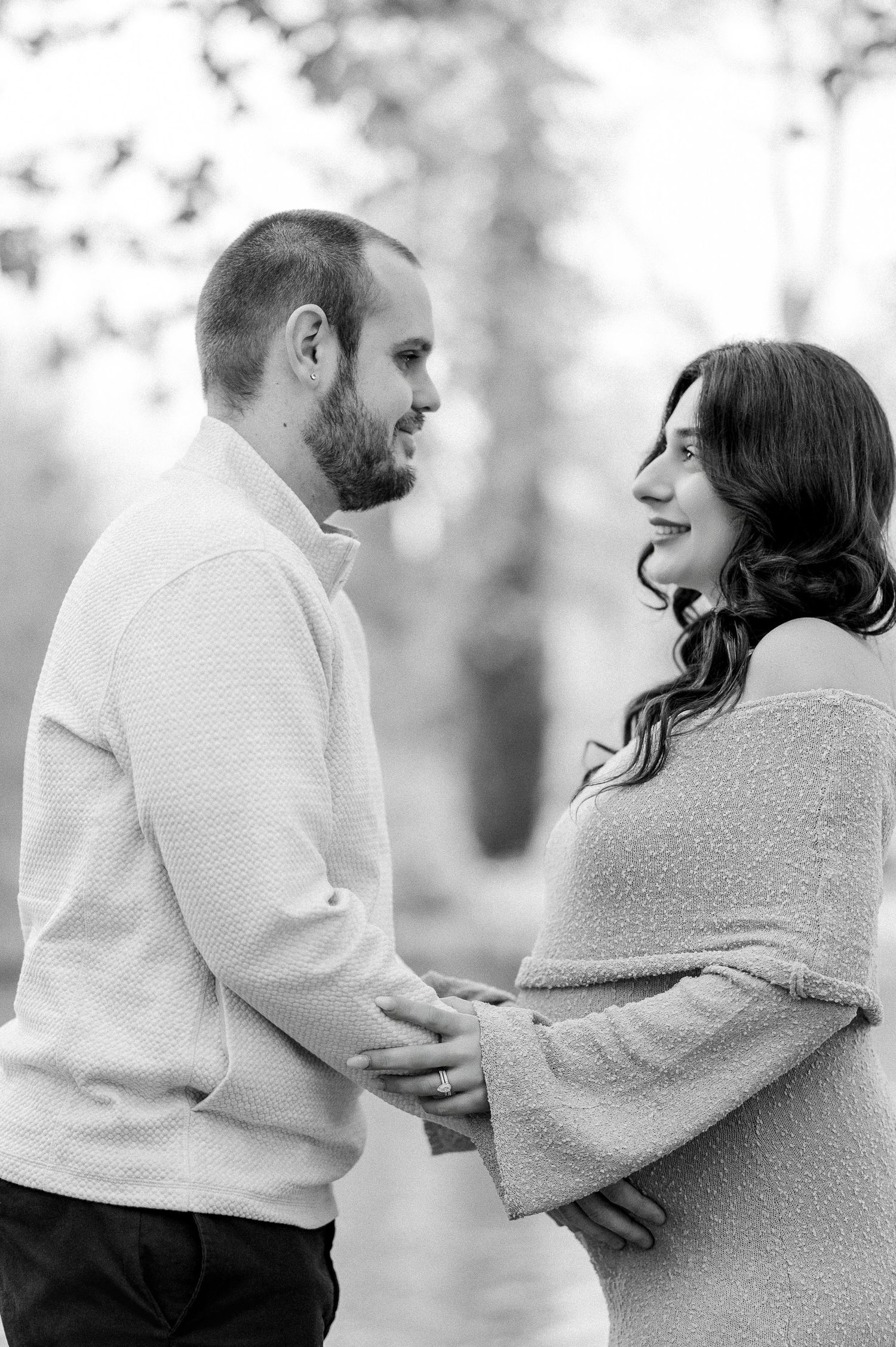 A romantic couple in white sweaters embrace lovingly during a black and white outdoor photoshoot.