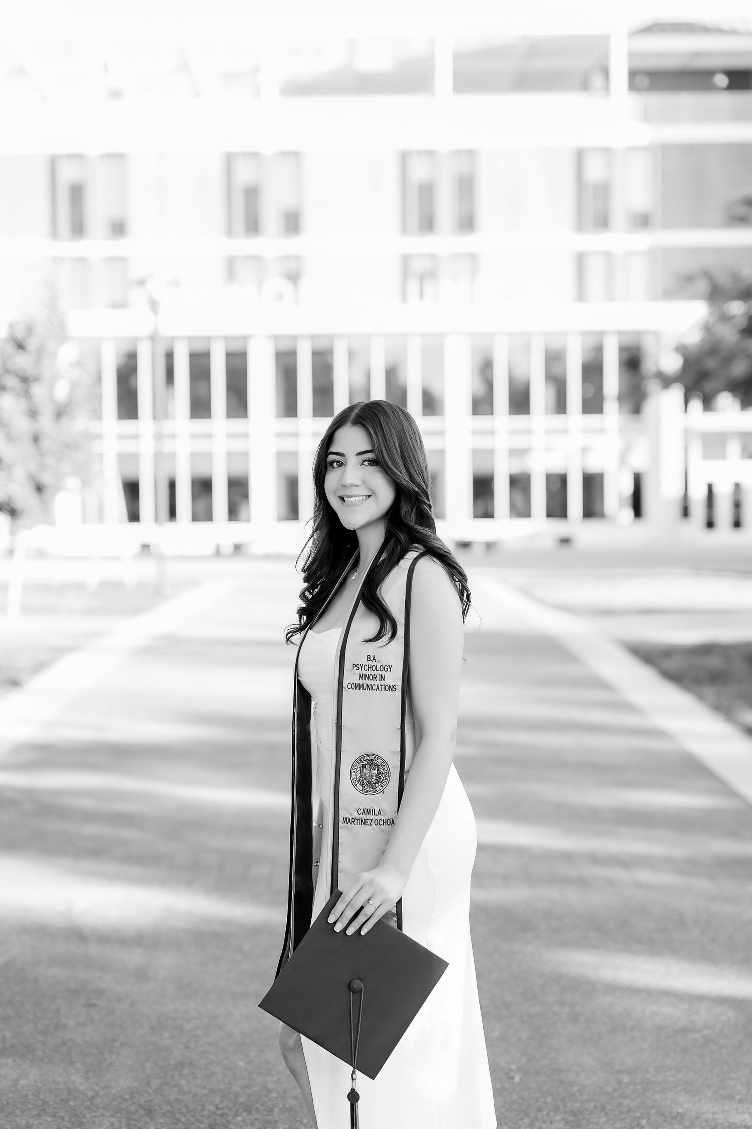 Black and white graduation portrait with graduate holding diploma and wearing honors sash.