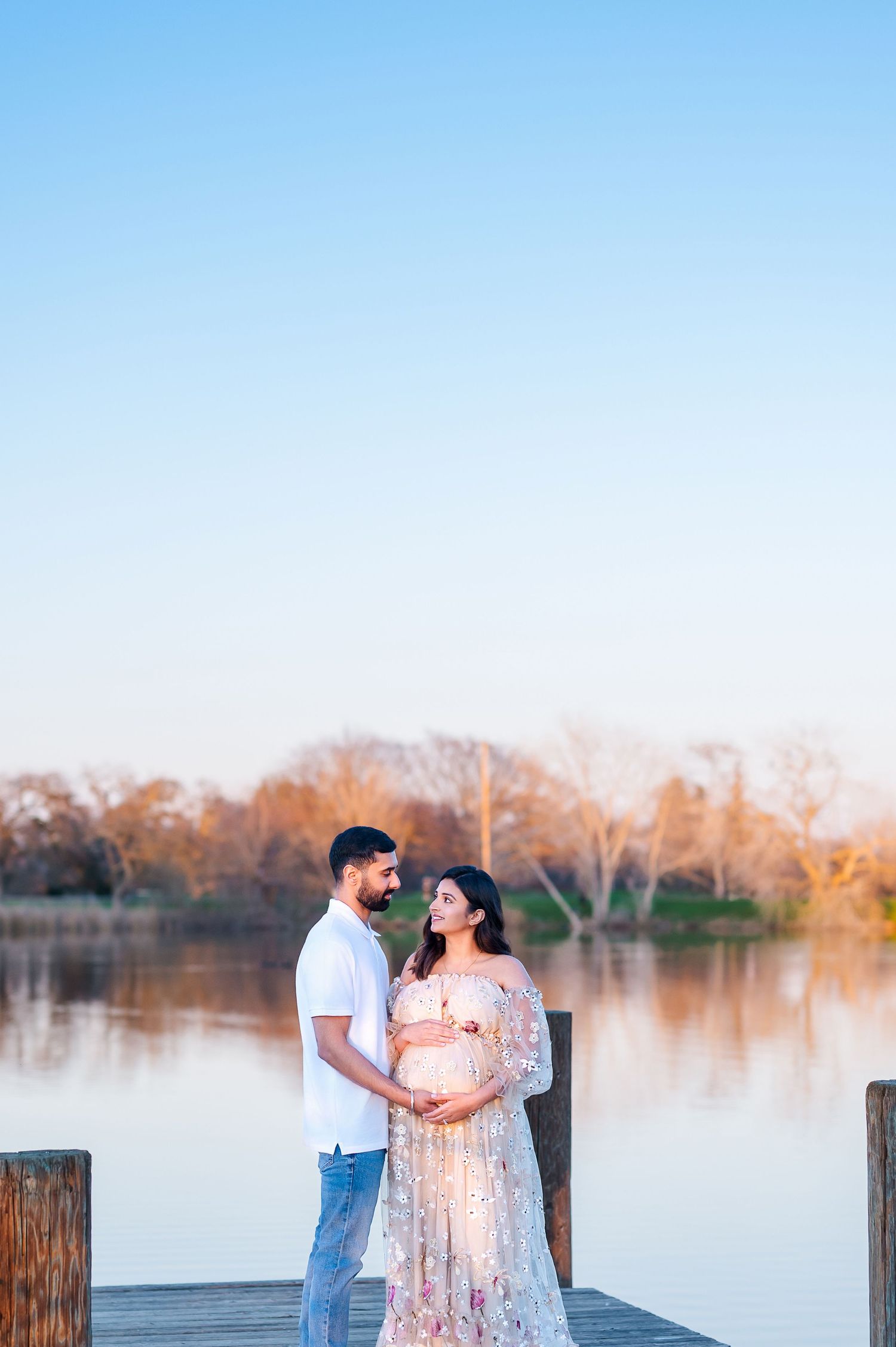 Waterfront maternity photography with couple on dock during golden hour.