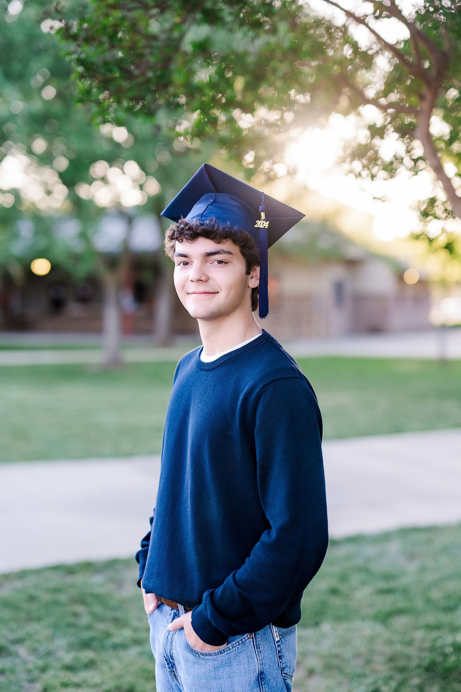 Graduate in blue cap against blurred natural background at sunset.