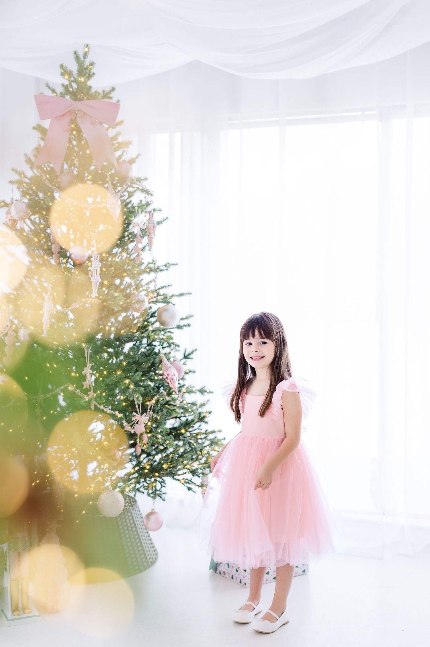 A dreamy photo series featuring a pink tulle dress against a white backdrop with soft natural lighting and greenery accents.