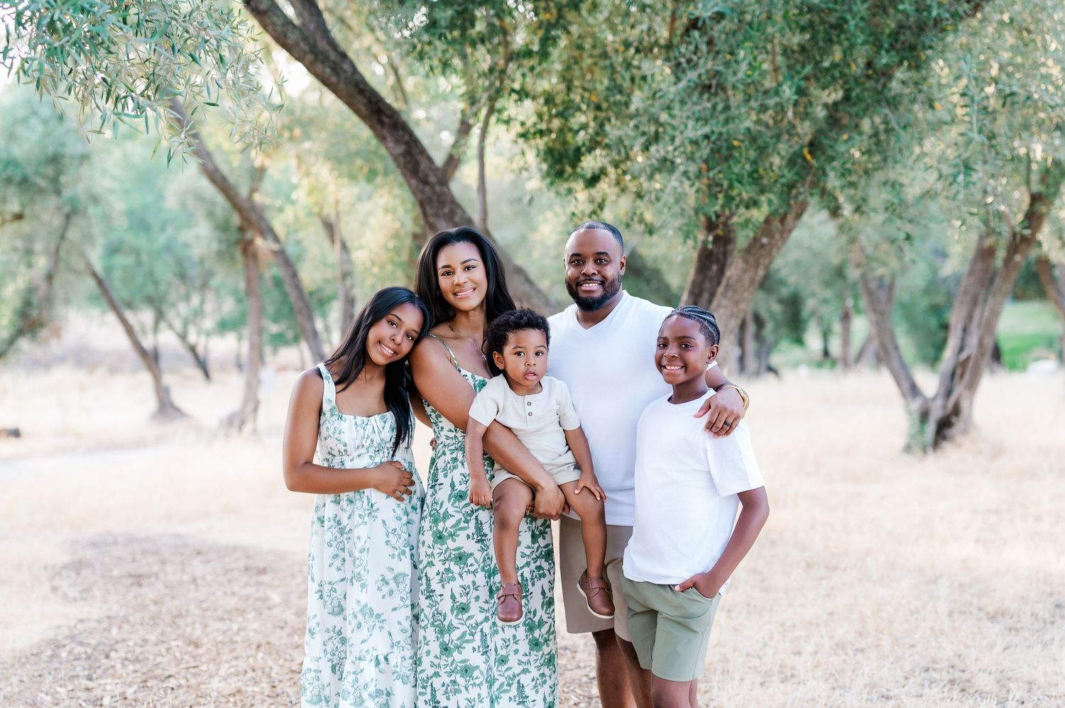 A group of people enjoying a casual outdoor photo session in a sun-dappled grove of trees.