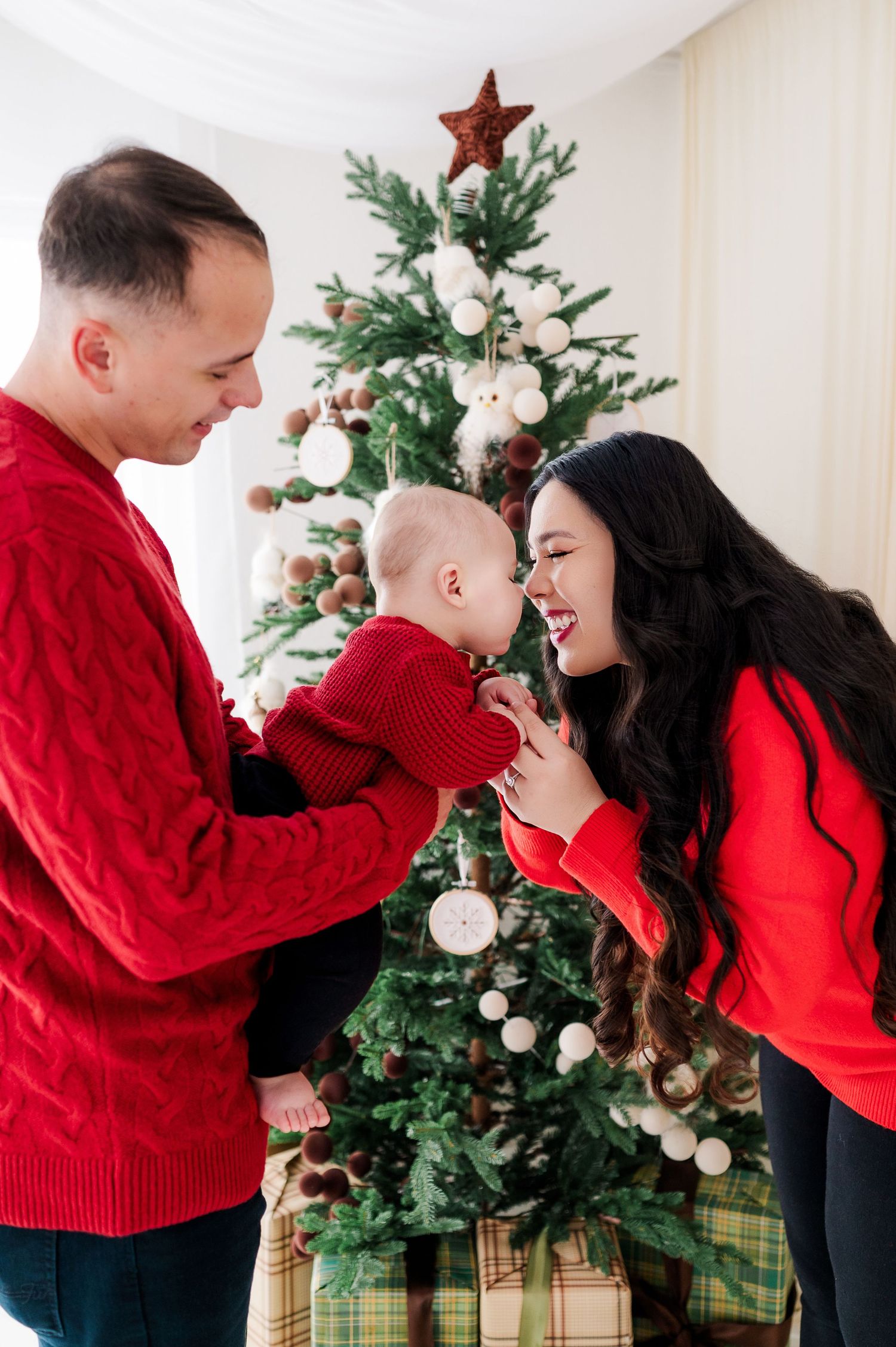 A couple in matching red sweaters share tender moments in front of a decorated Christmas tree in a photo series.