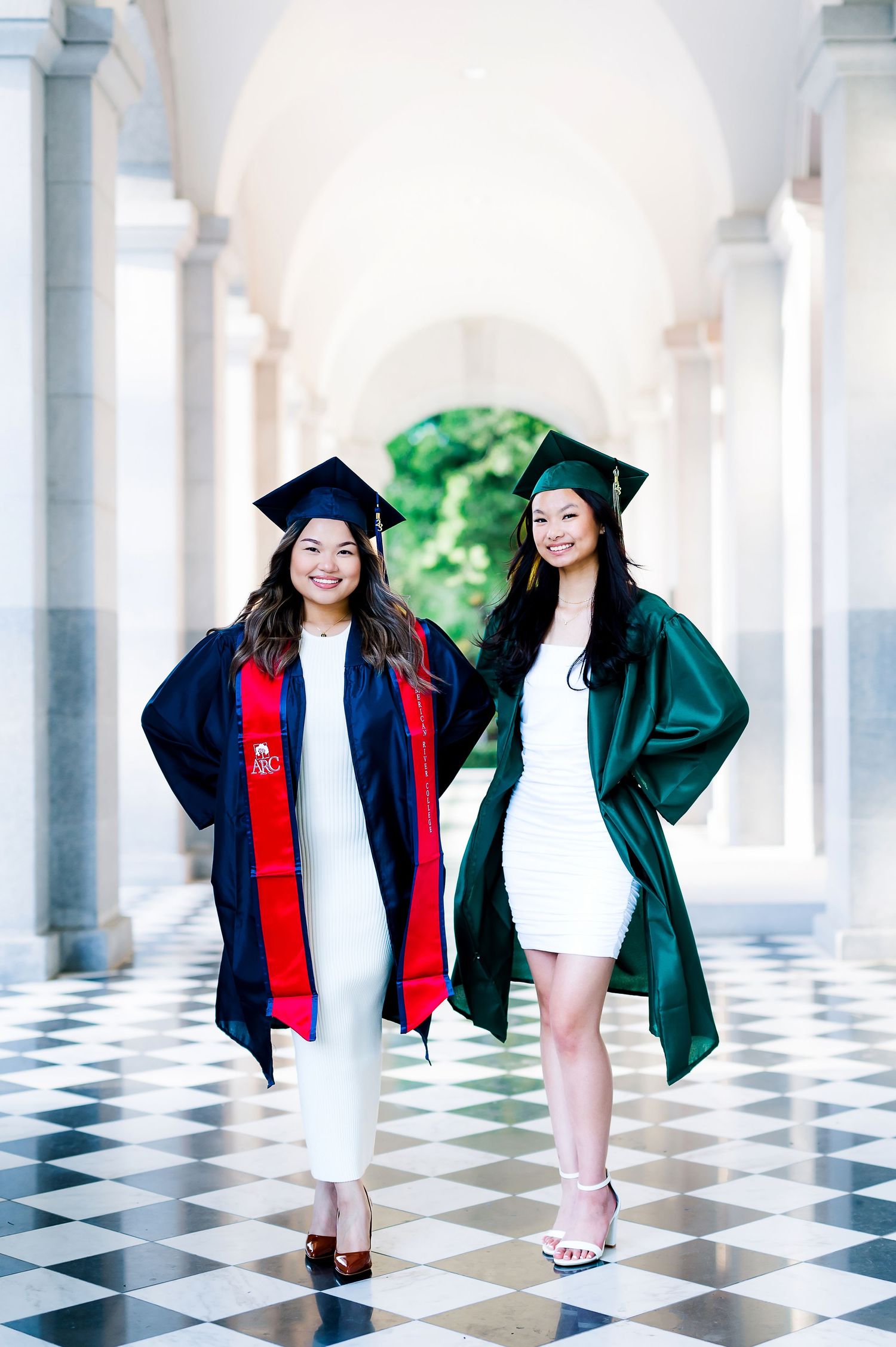 Graduates in cap and gowns pose playfully on black and white checkered floor.