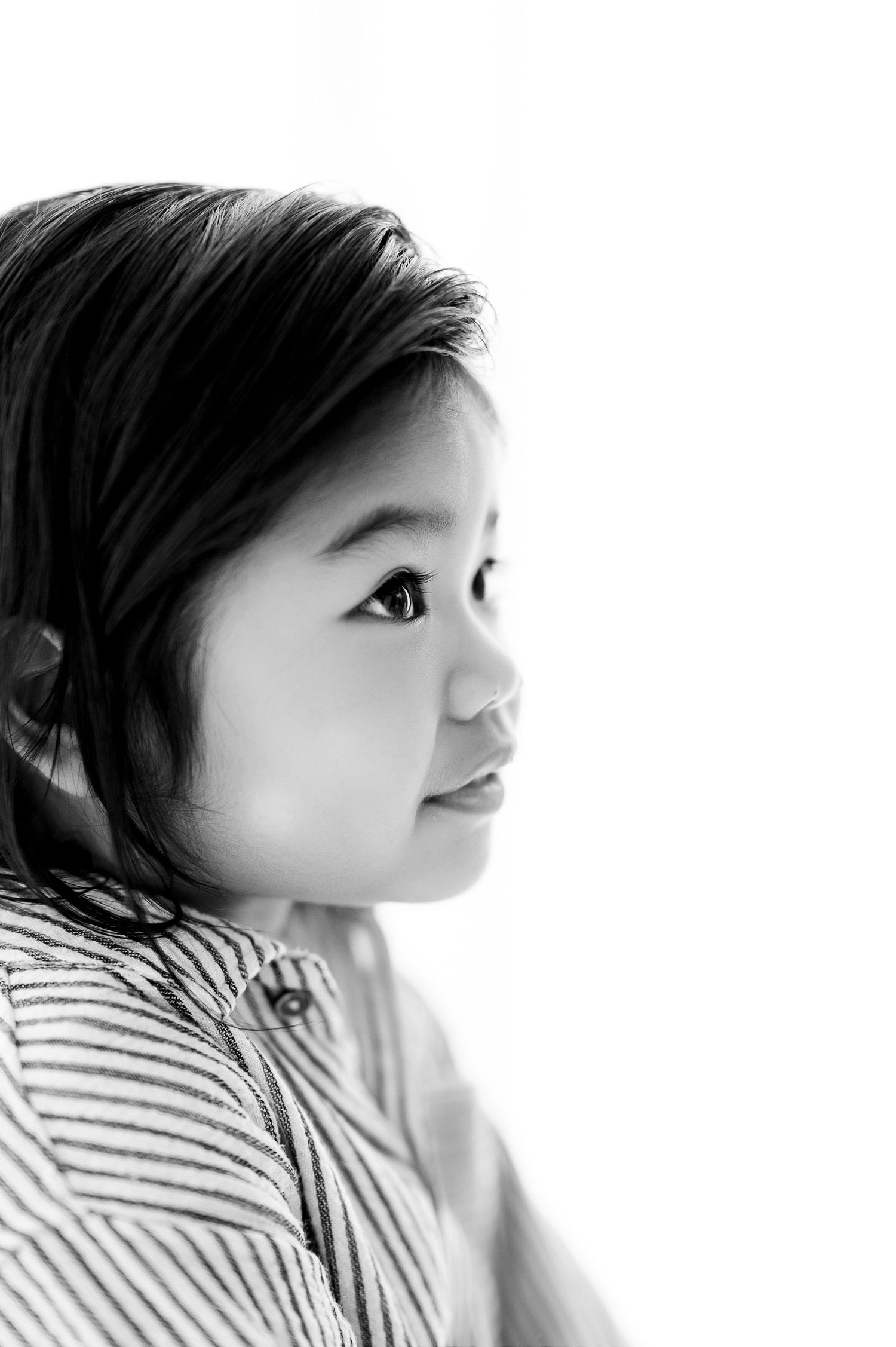 Black and white portrait of a young Asian boy in a striped shirt, gazing upward with a gentle smile.