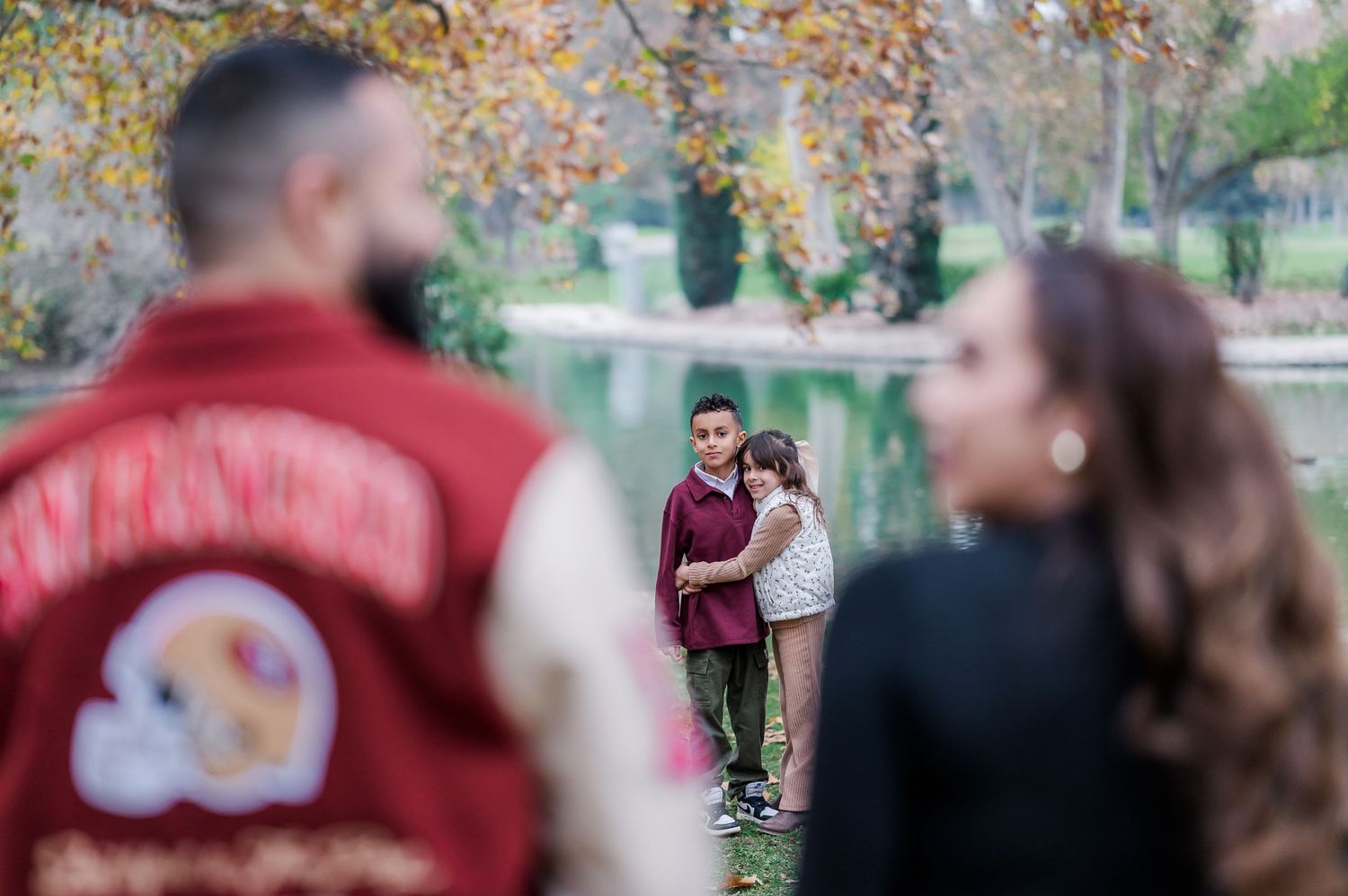 People gather in a park during autumn with colorful fall foliage visible in the trees above.