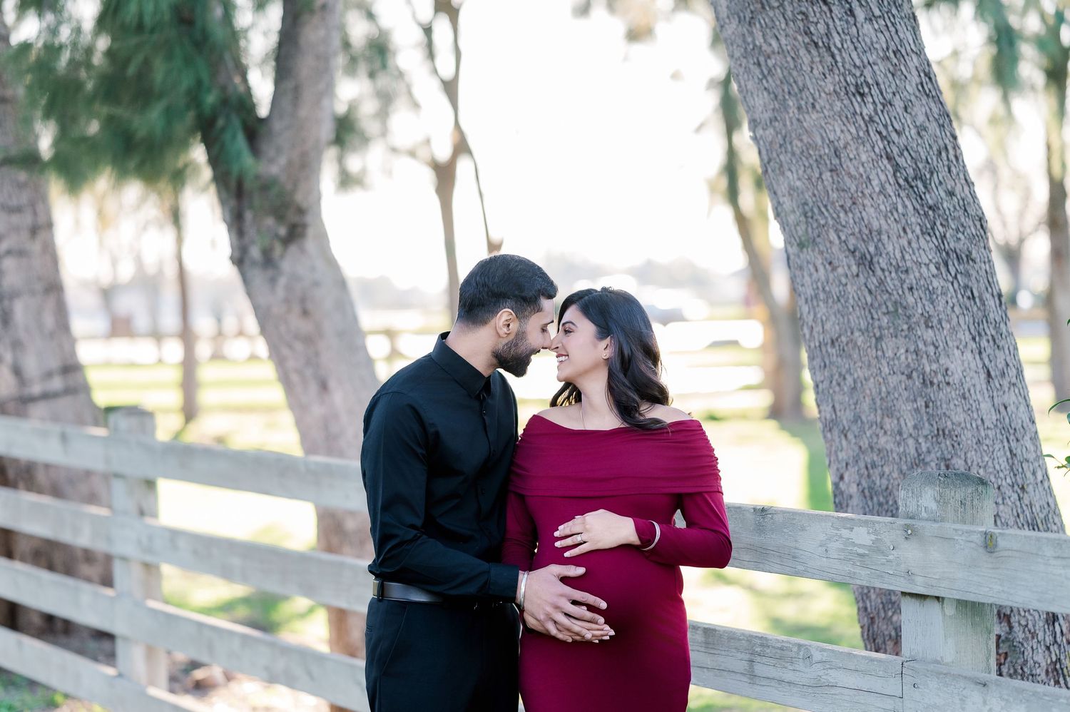 Romantic couple in formal attire share tender moments during outdoor photo session in wooded park setting.