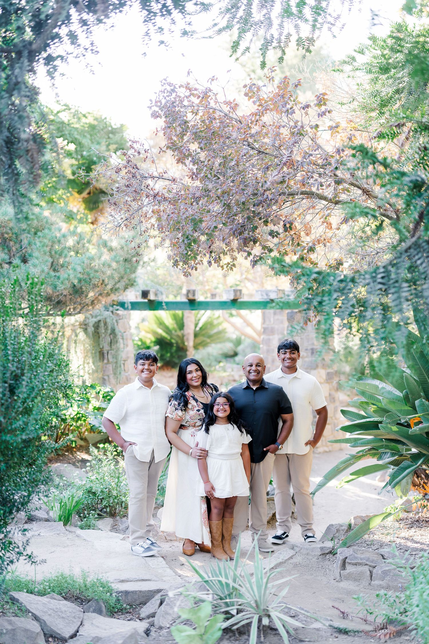 A group poses together on a garden path surrounded by lush greenery and trees in a beautiful outdoor setting.