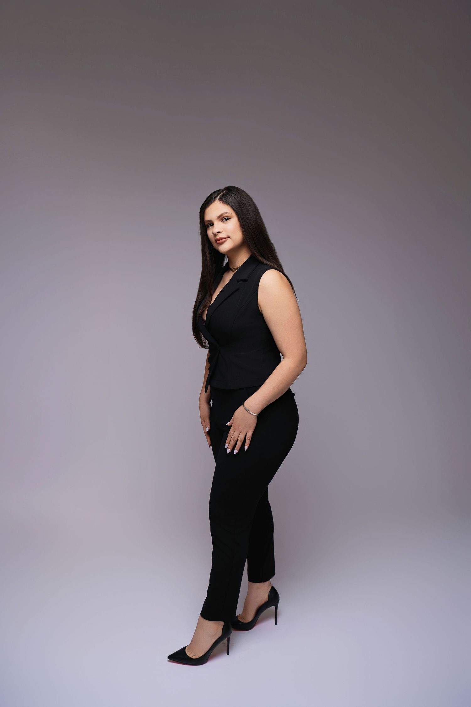 Professional portrait of a woman in a sleek black outfit posing against a gray background.