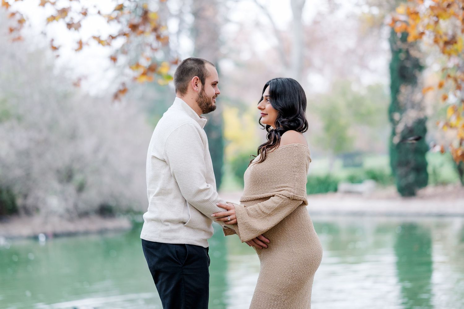 A couple in autumn attire shares intimate moments by a lake surrounded by fall foliage and mist.